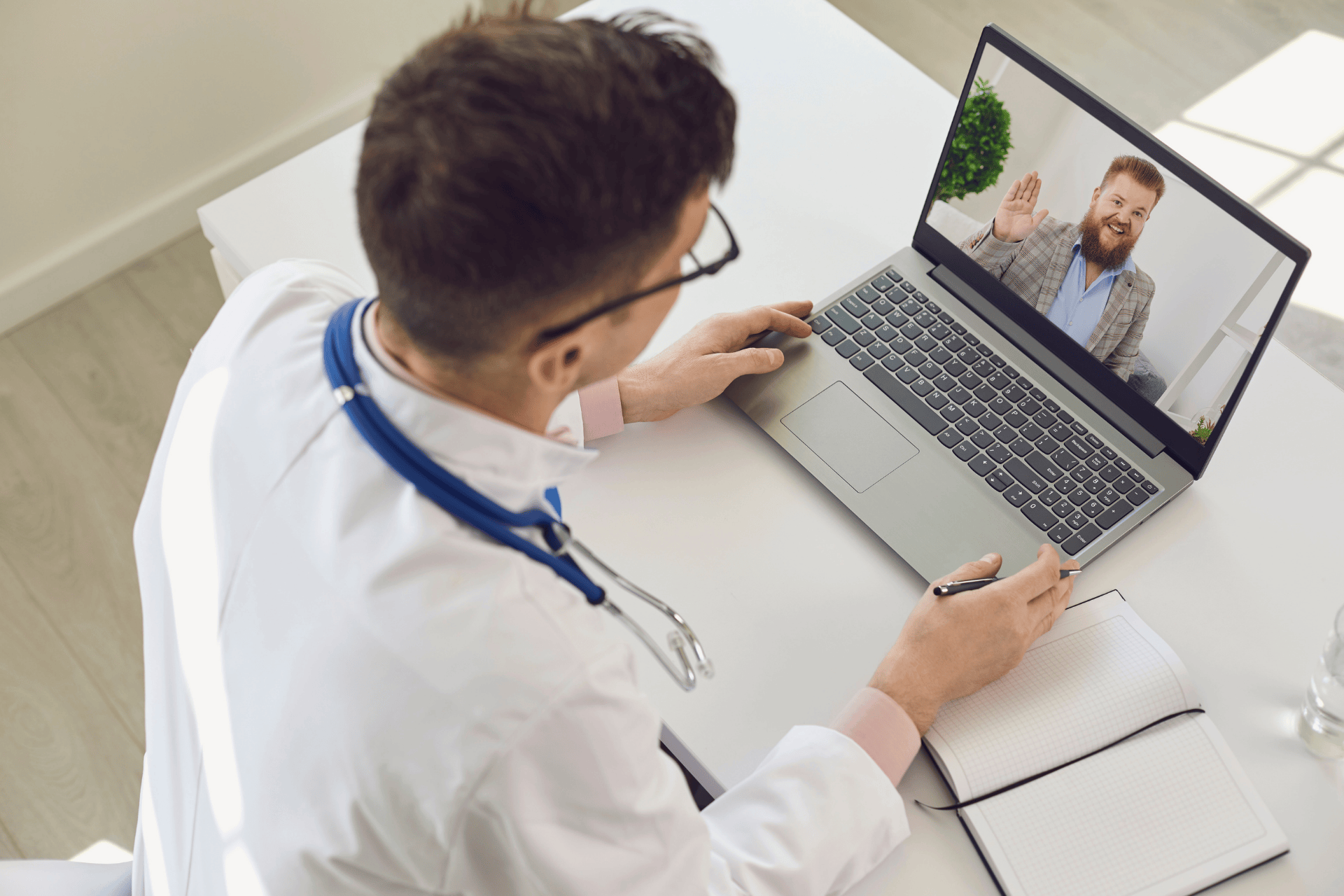 Doctor having an online video consultation with a male patient waving on a laptop screen.