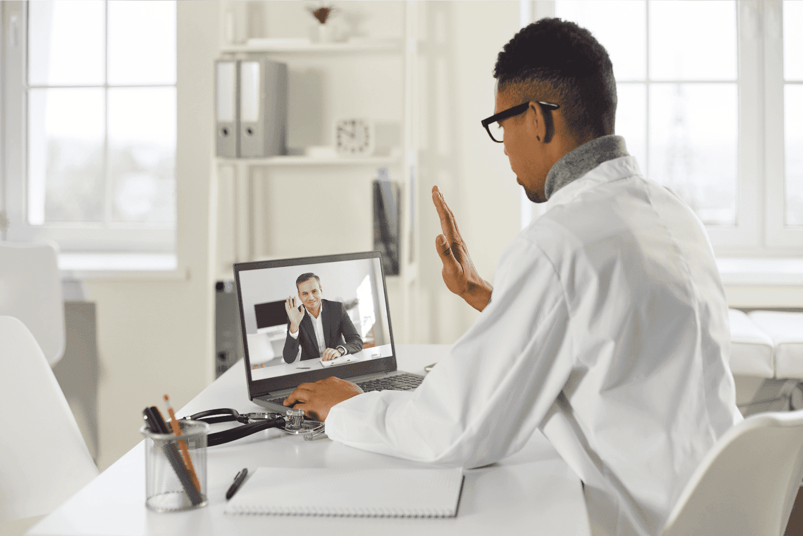 Doctor in a white coat having a video call with a patient on a laptop in a medical office