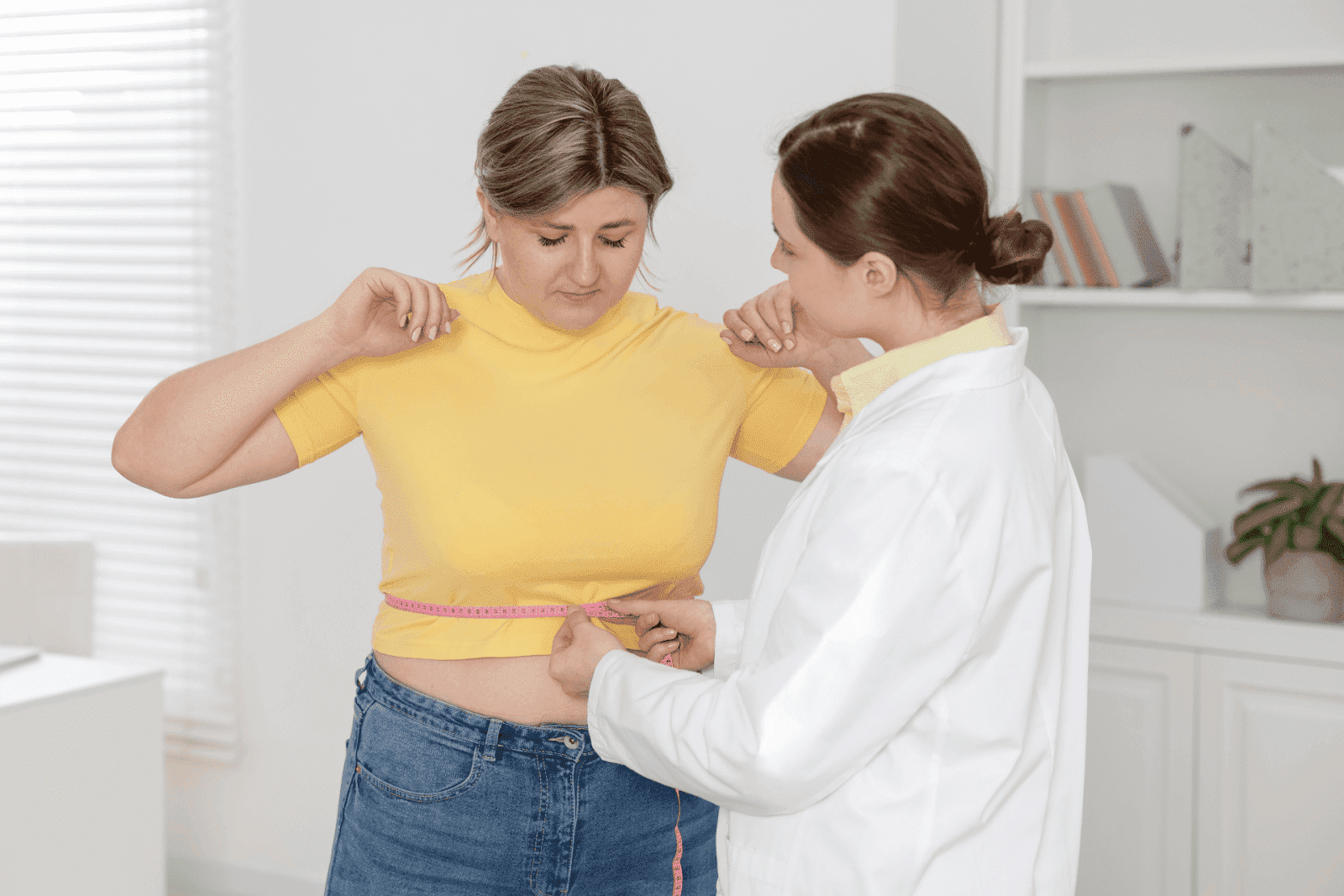 Doctor measuring a woman’s waist with a tape measure during a consultation.