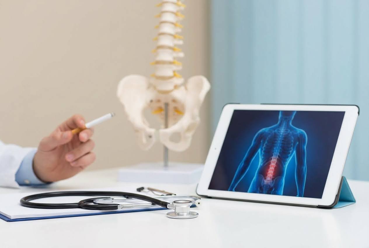 Doctor's hand holding a cigarette, with a spine model and a tablet displaying a human torso with a red lower back.