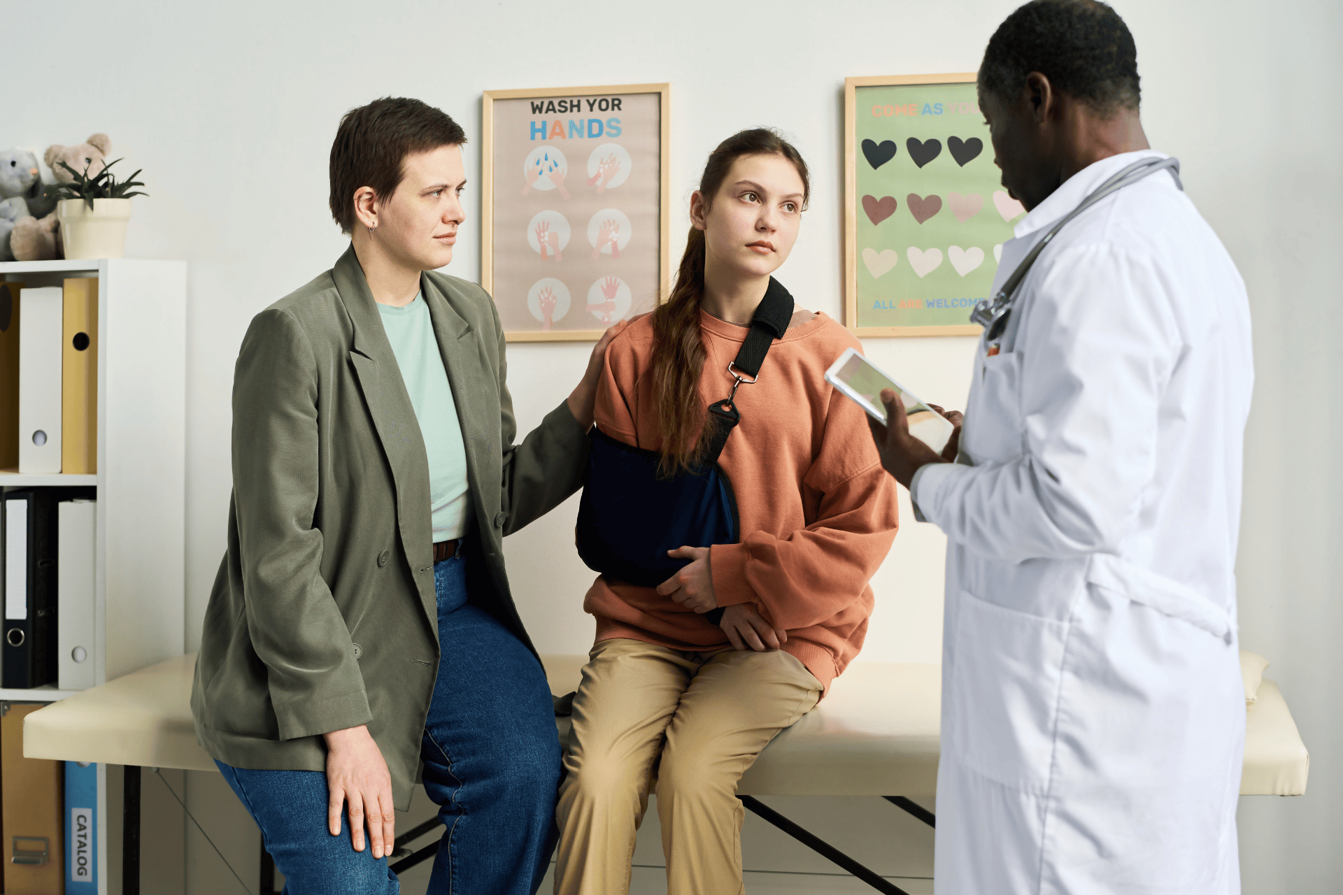 Doctor talking with a teenage patient wearing an arm sling and a concerned parent in a clinic.