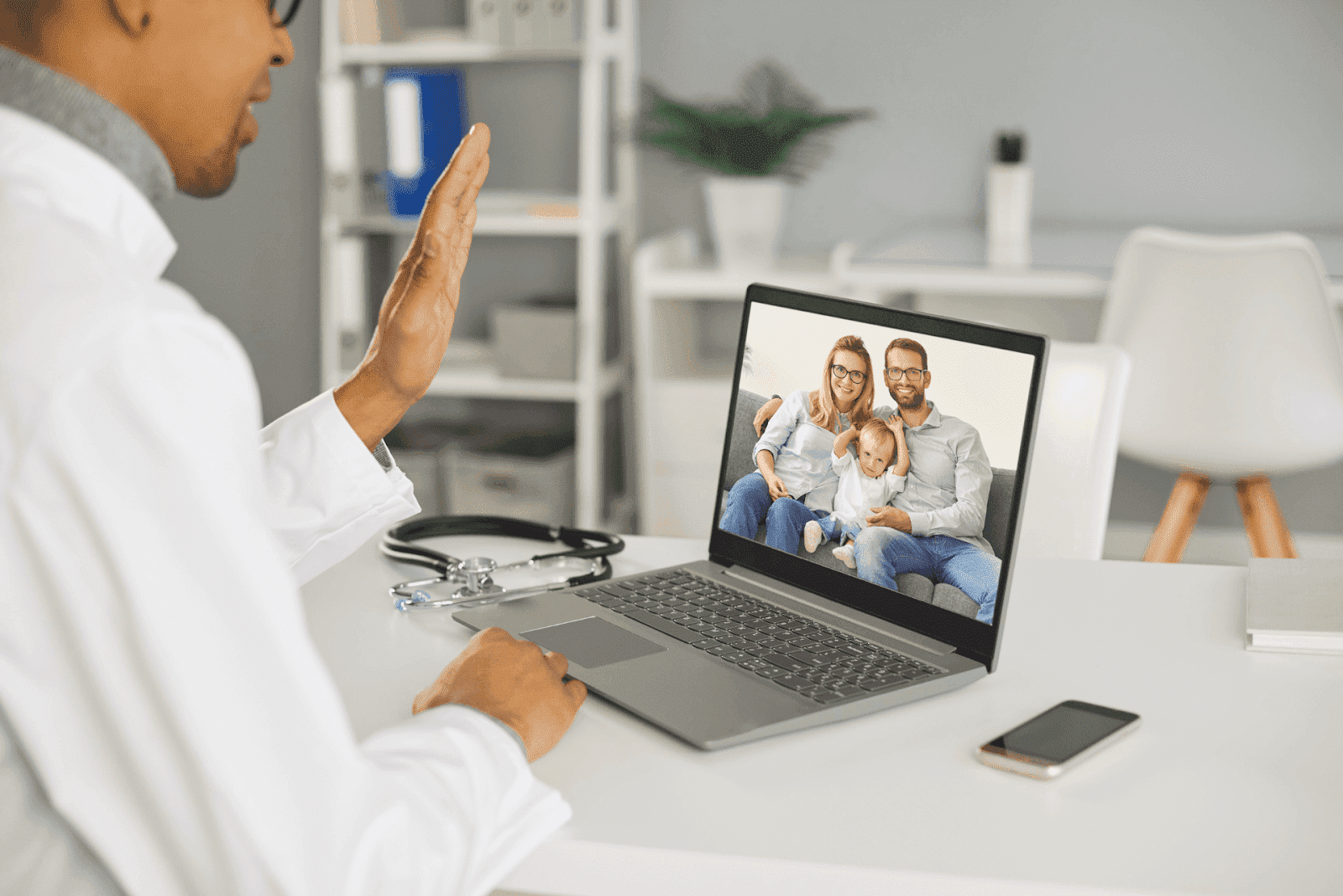 Doctor waving at a family on a laptop screen during a telehealth video call.