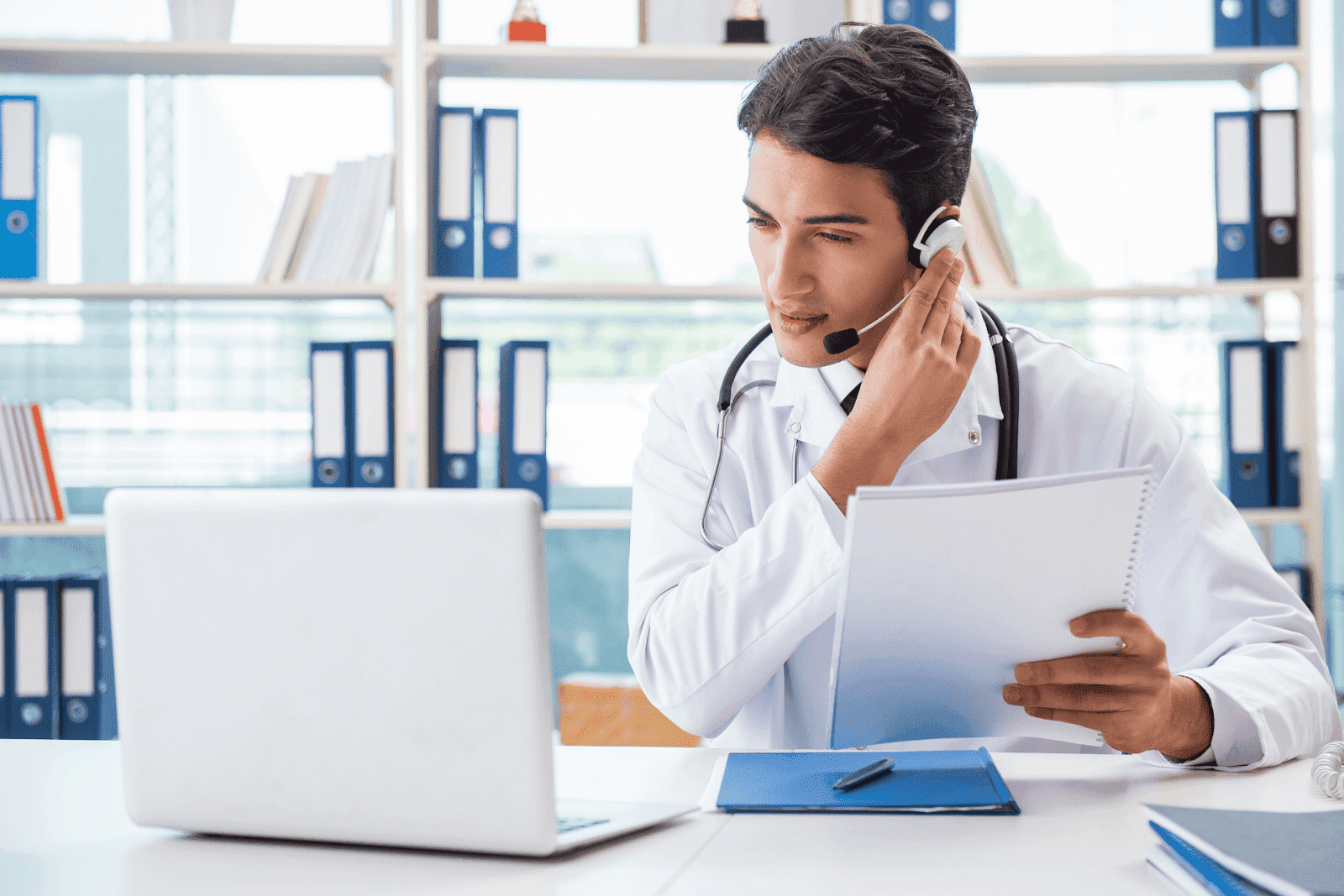 Doctor wearing a headset talking to a patient online while holding notes.