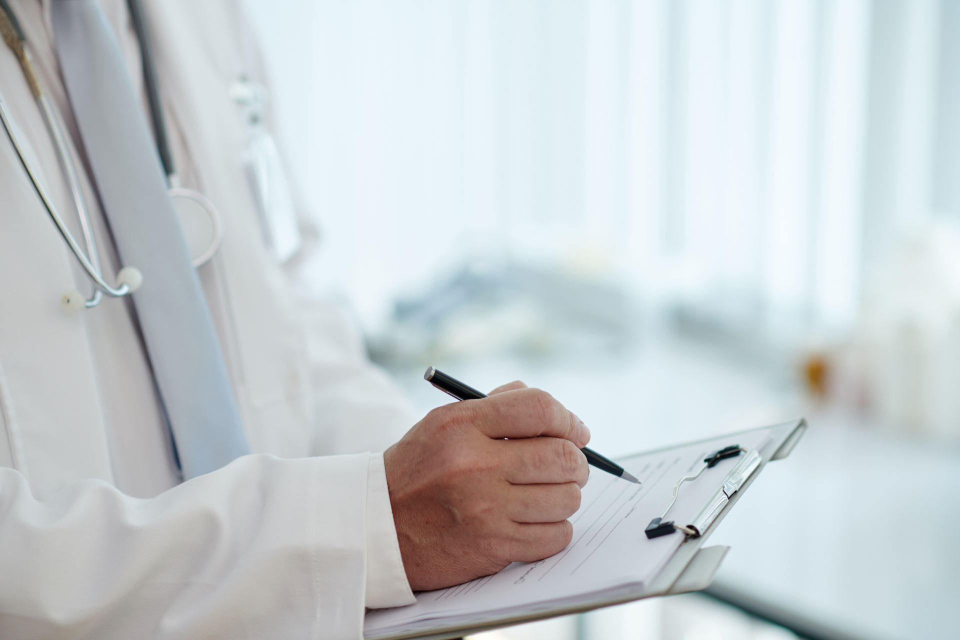 Doctor writing notes on a clipboard in a bright clinical setting