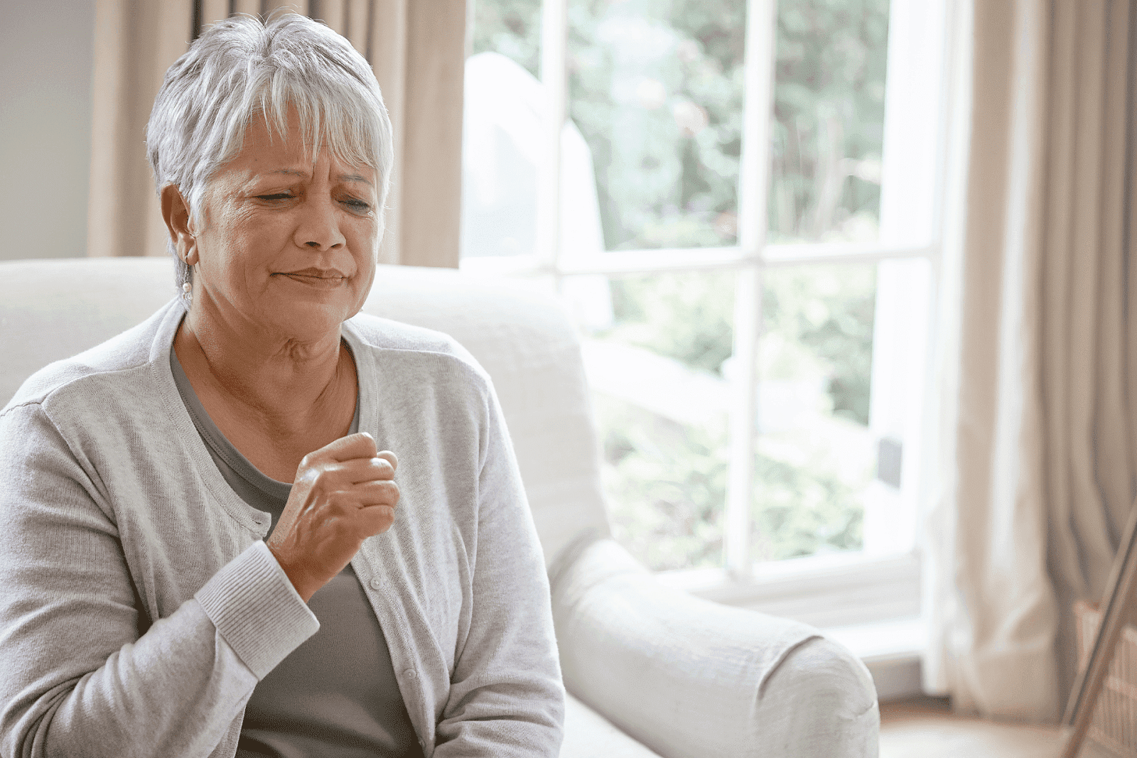 Elderly woman coughing while sitting on a couch.