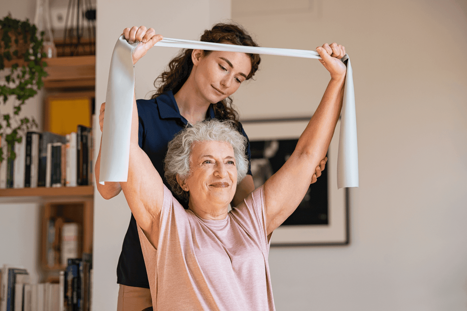 Elderly woman doing exercises with a resistance band, assisted by a young female physiotherapist.