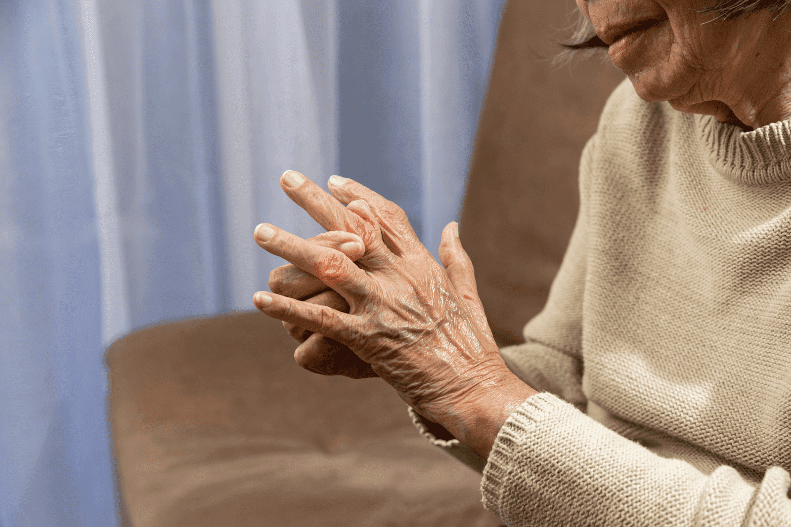 Elderly woman holding her painful, inflamed fingers with visible joint reddness