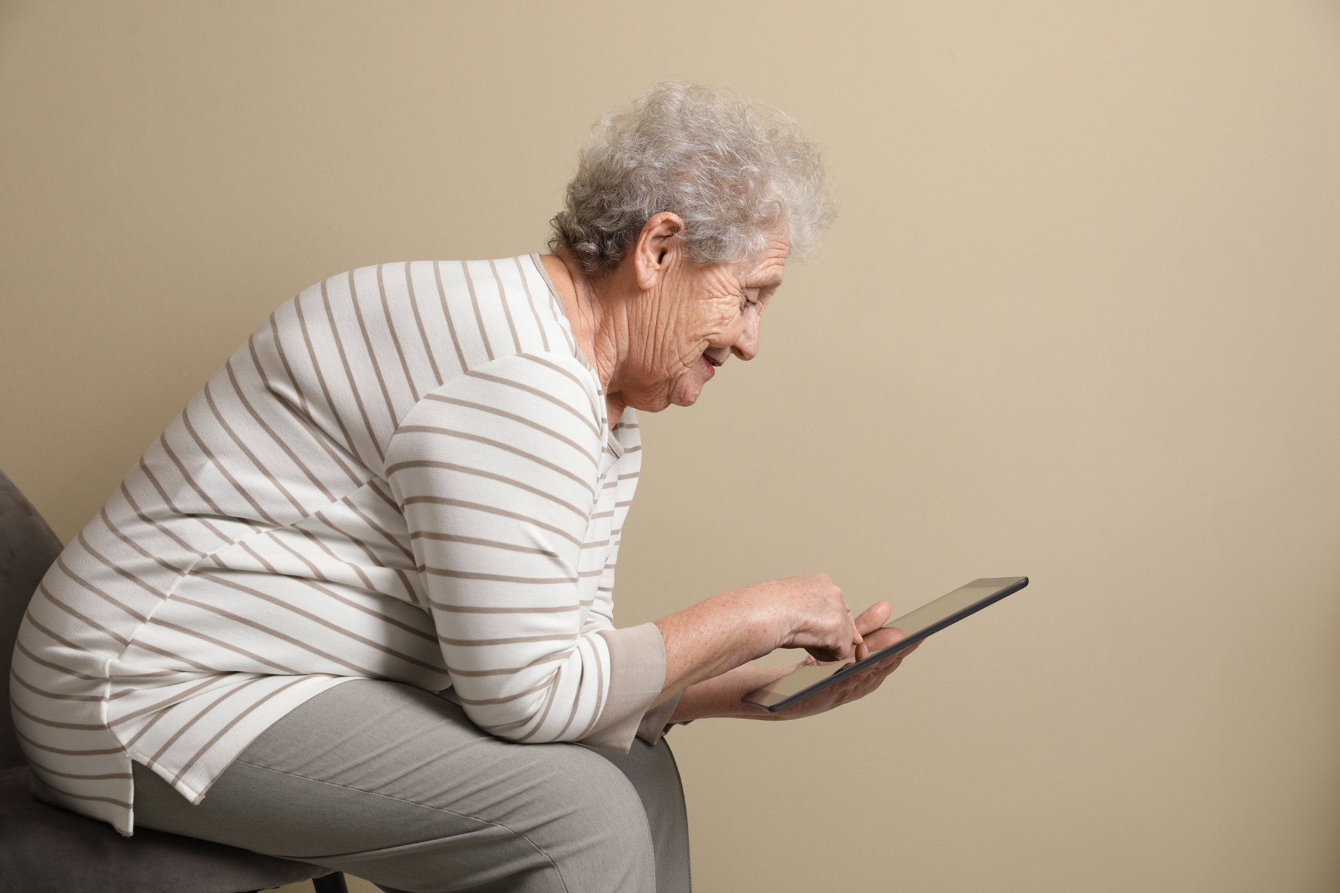Elderly woman sitting hunched over while using a tablet