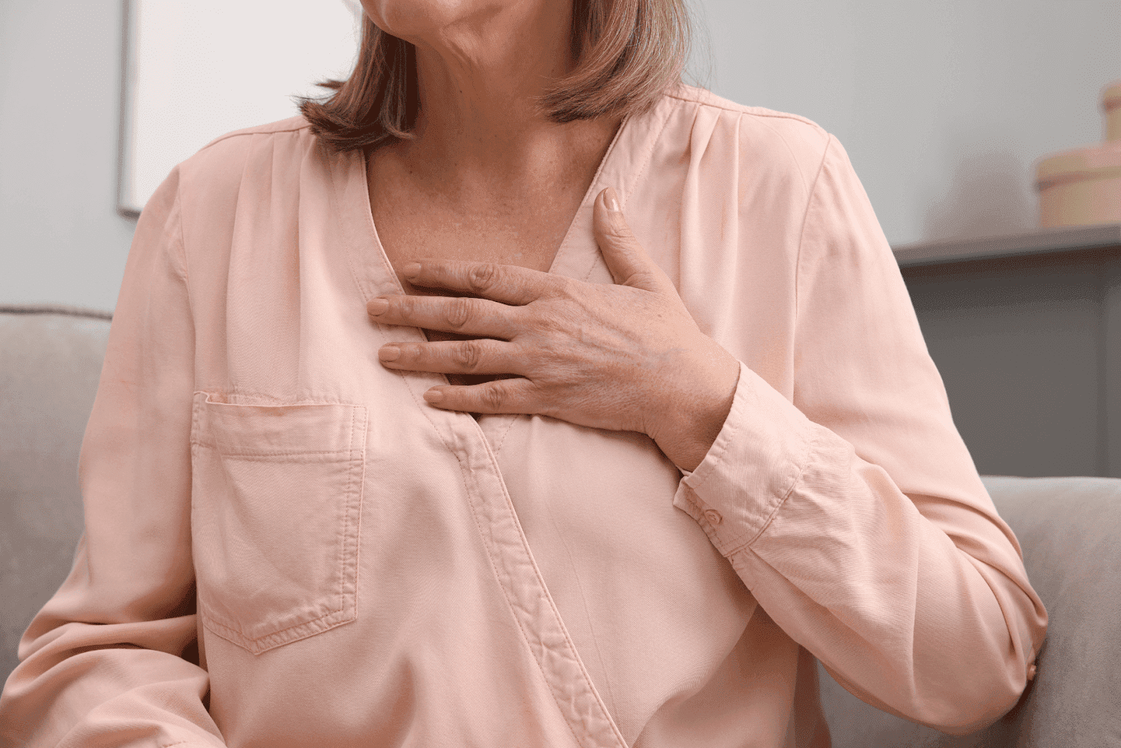 Elderly woman touching her chest while seated, suggesting possible chest pain.