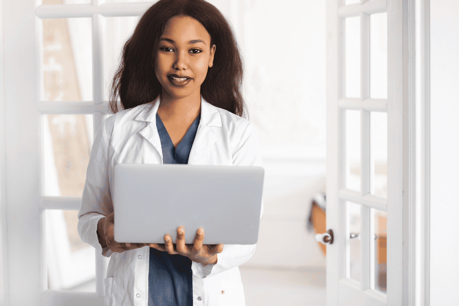 Female doctor holding a laptop and smiling in a bright office.