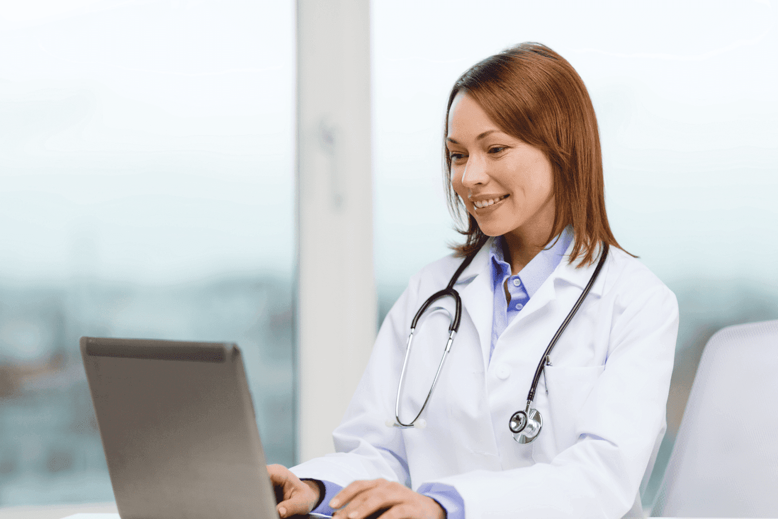 Female doctor smiling while working on a laptop.