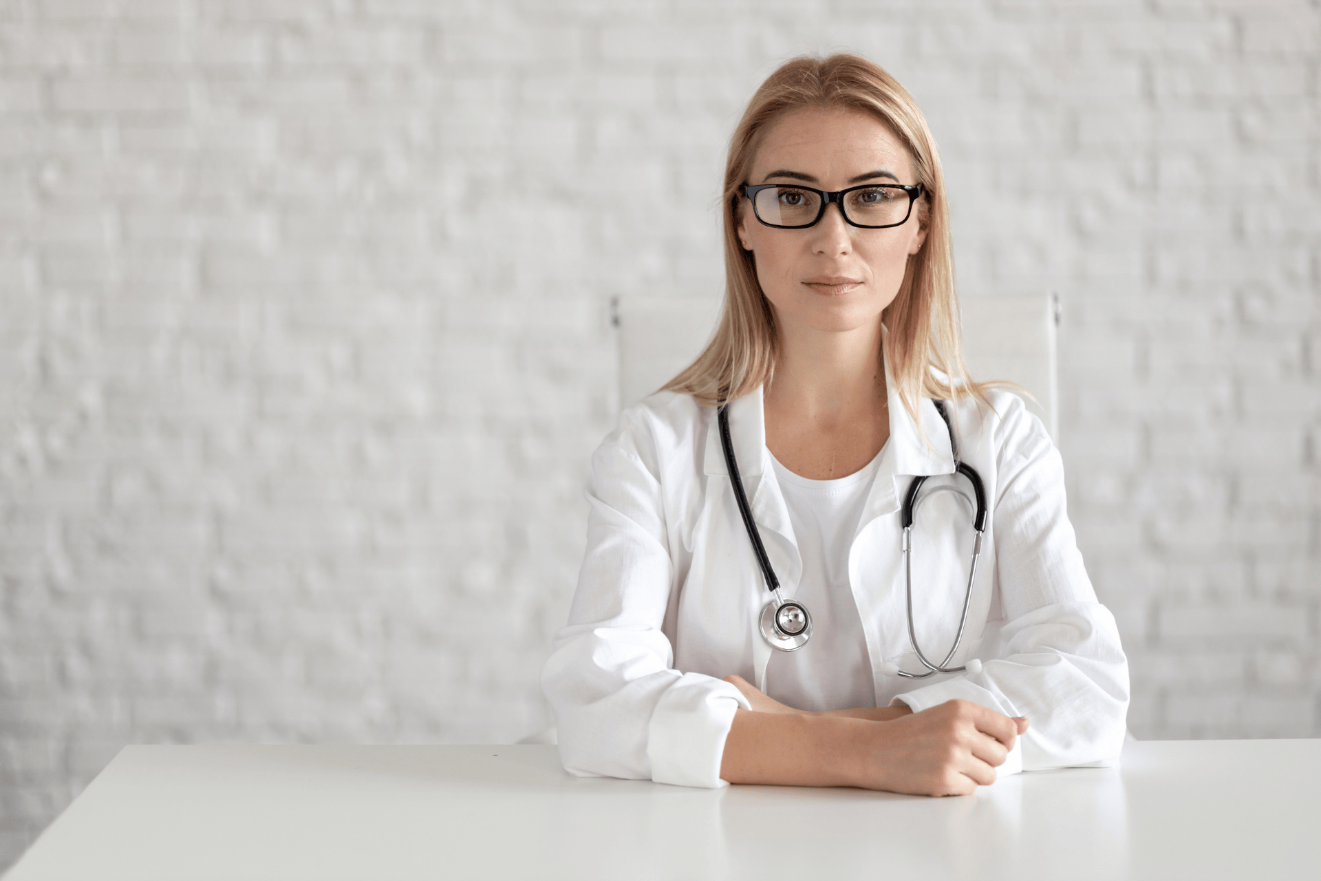 Female doctor with glasses sitting at a desk and looking forward.