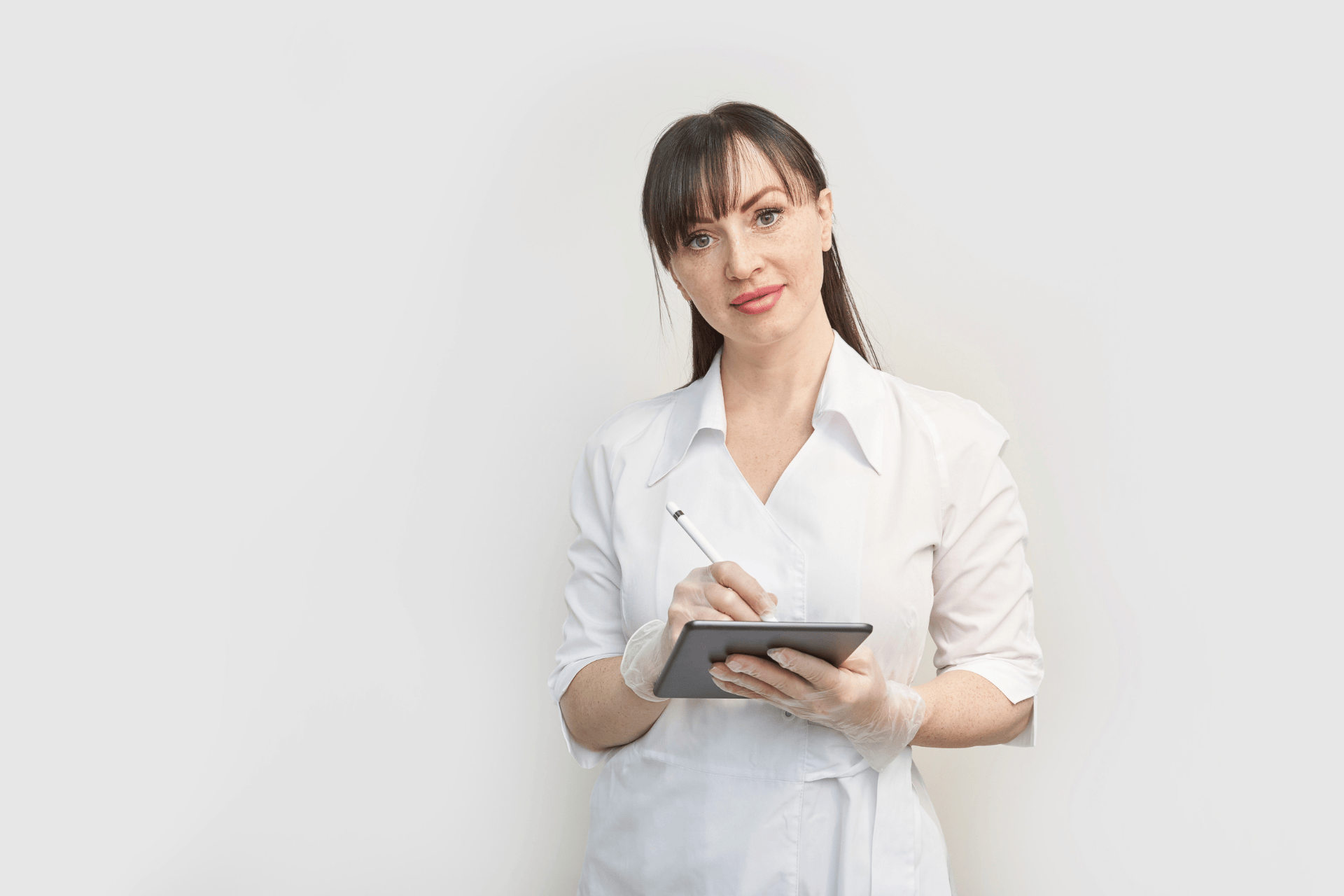 Female healthcare professional in a white coat holding a tablet and stylus, looking at the camera.