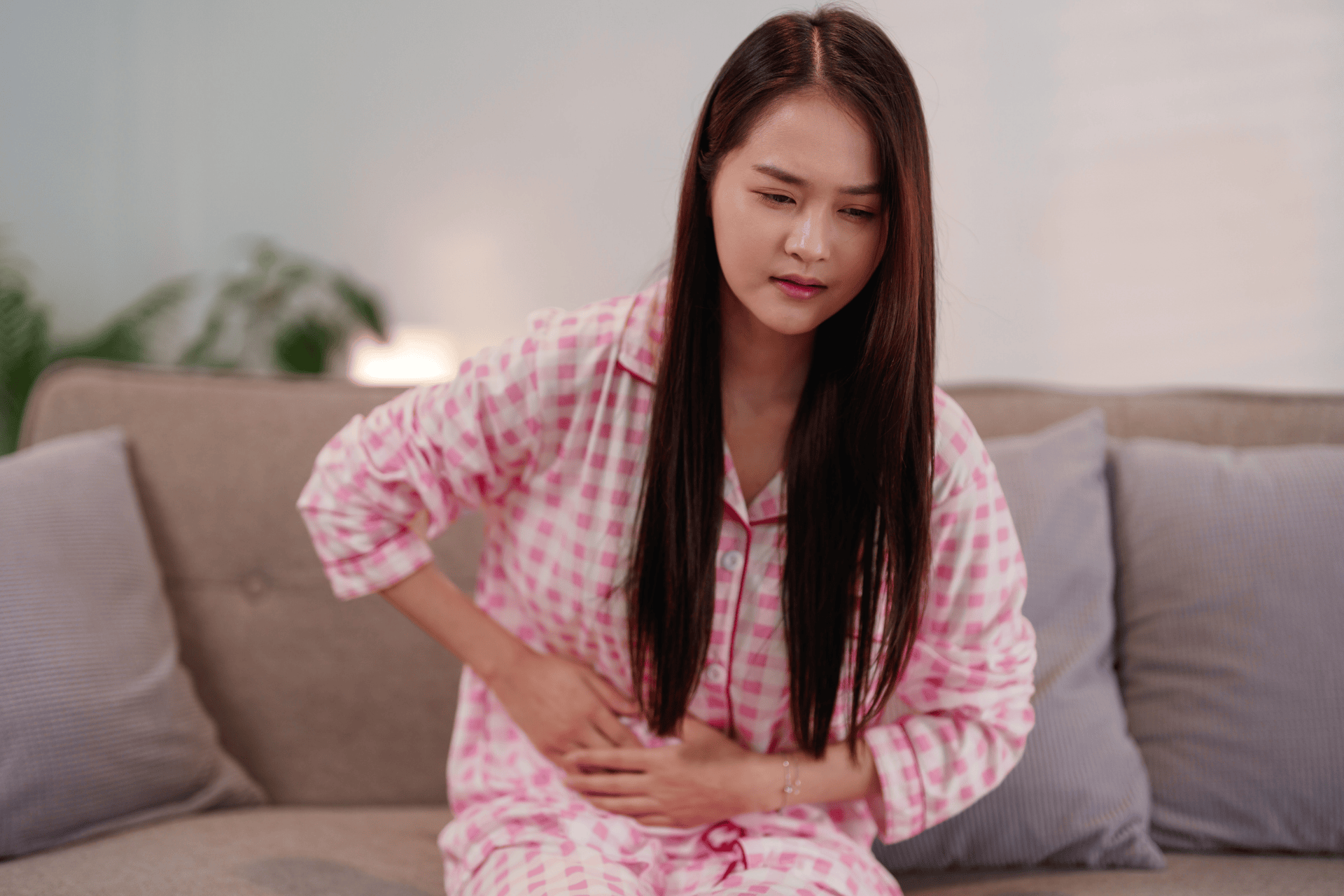 Woman sitting on a couch holding her stomach in pain.