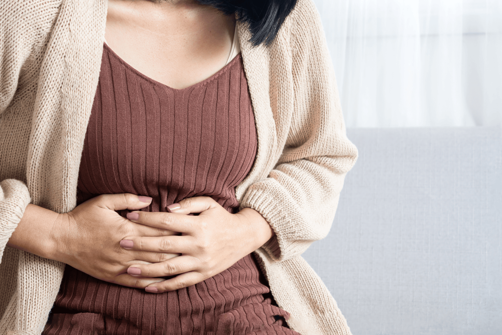 Woman clutching her stomach in discomfort while sitting on a couch.