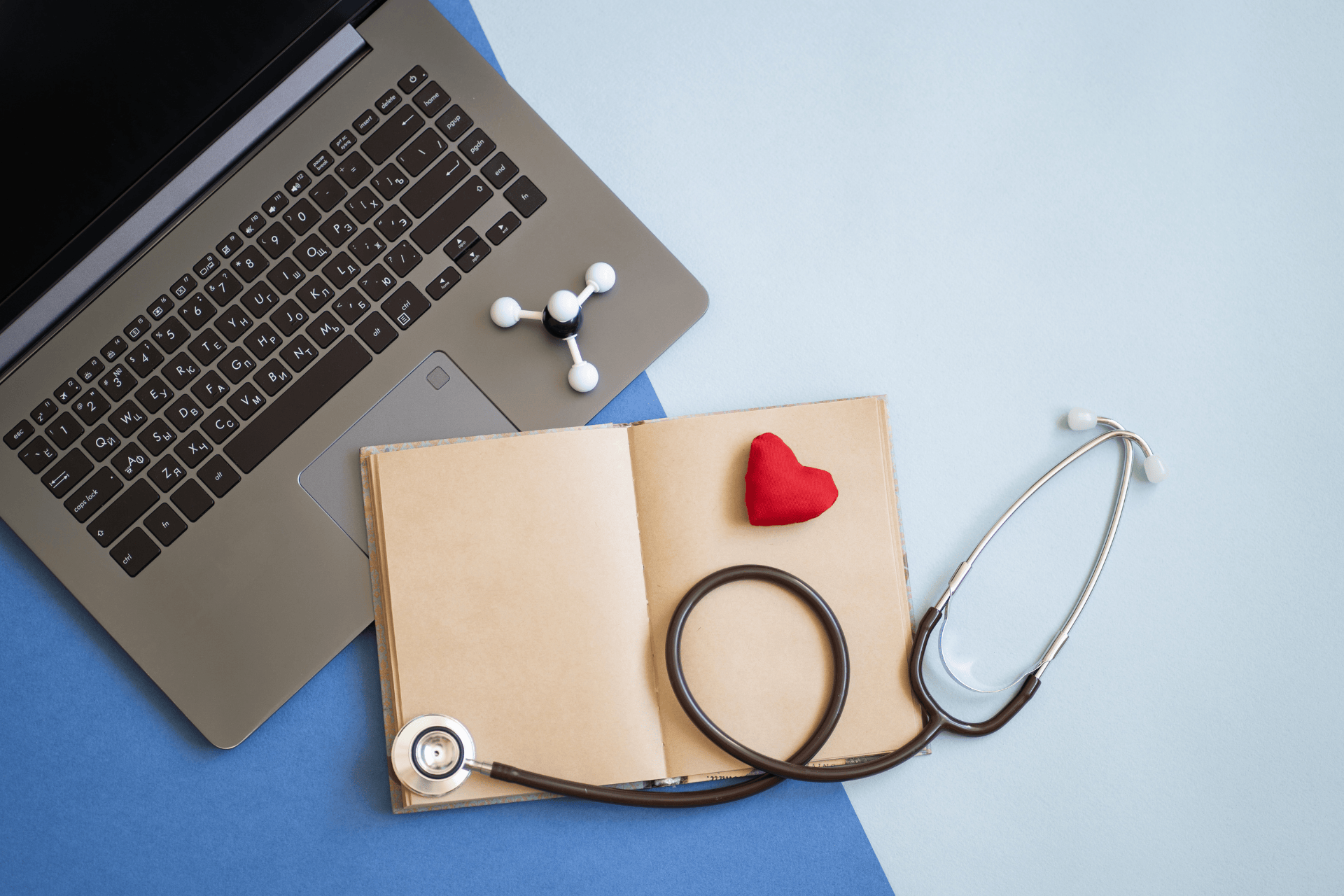 Laptop, stethoscope, and notebook with a small red heart on a desk.