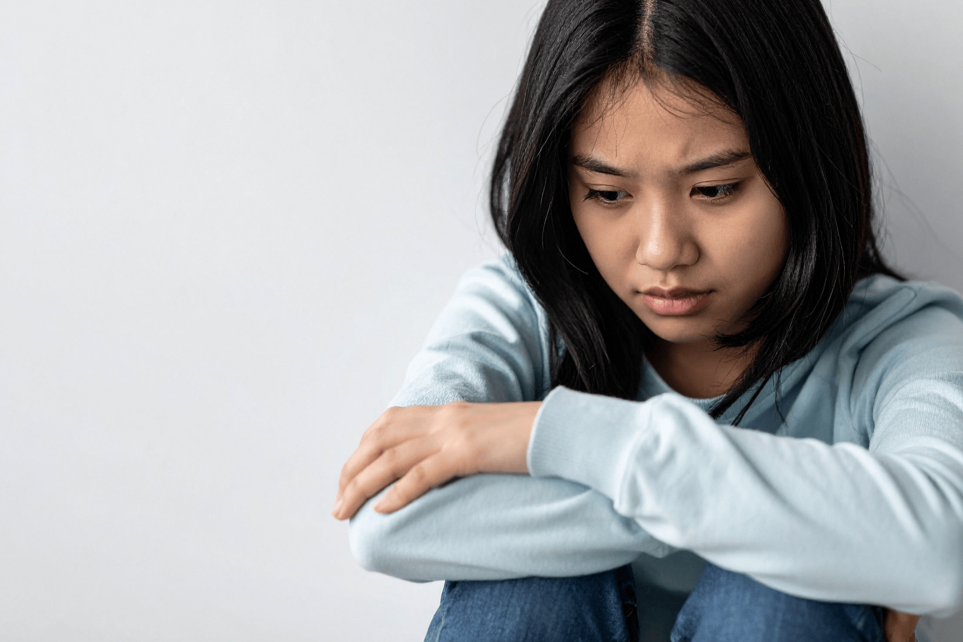 Sad girl sitting with arms crossed, looking down.