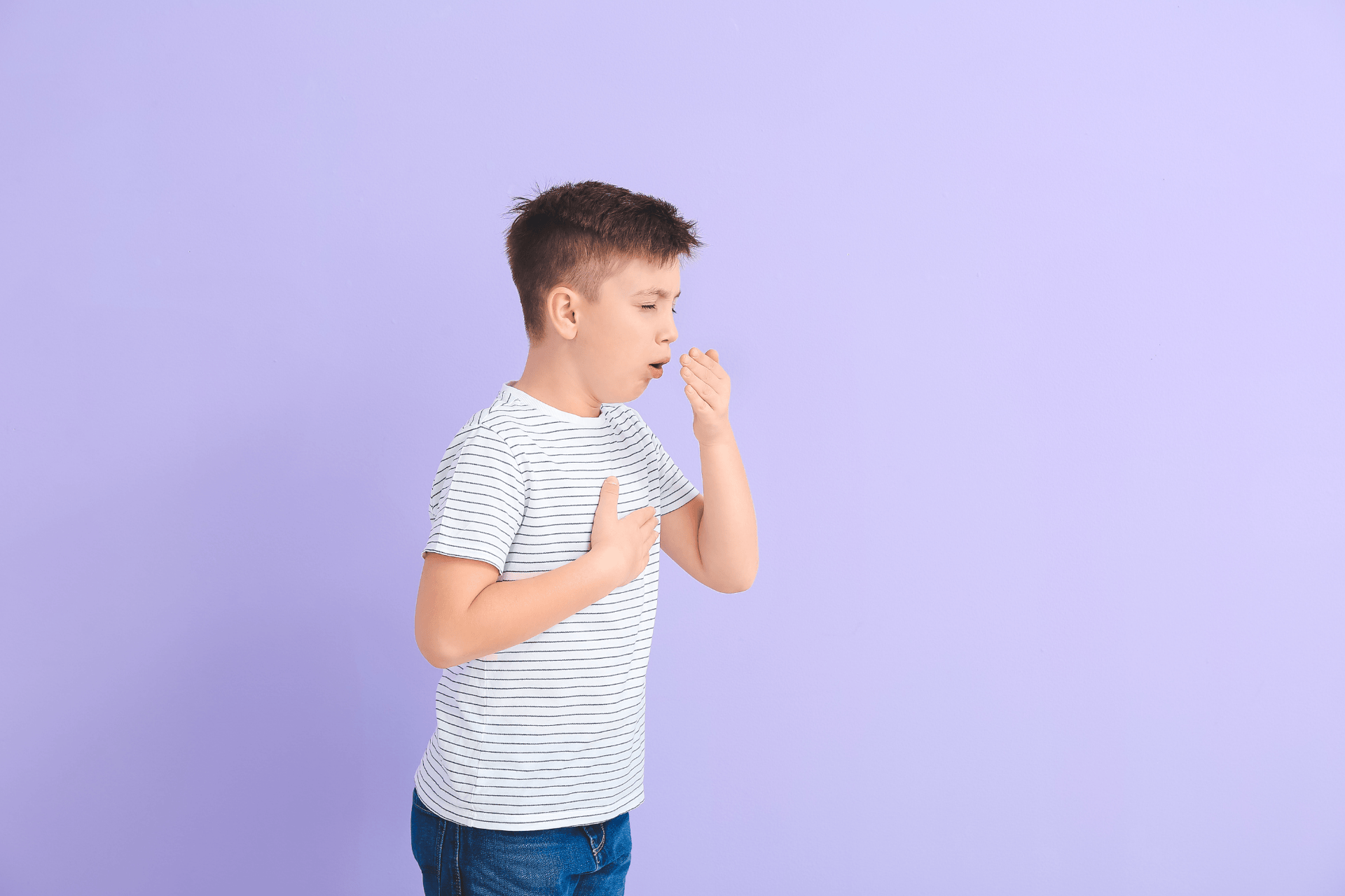 A young boy coughing into his hand against a purple background.