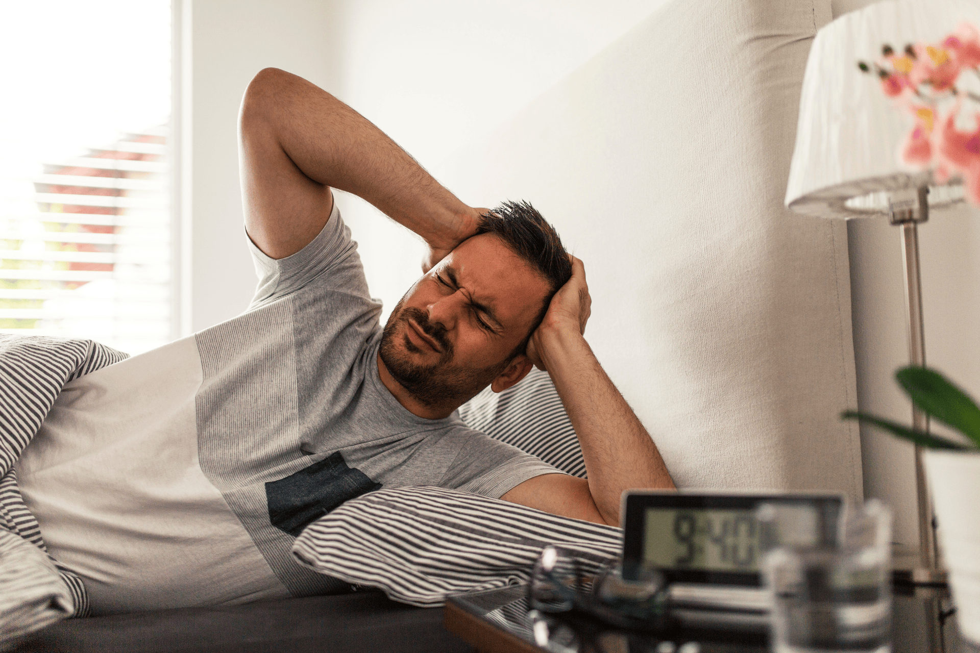 Man lying in bed holding his head in pain.