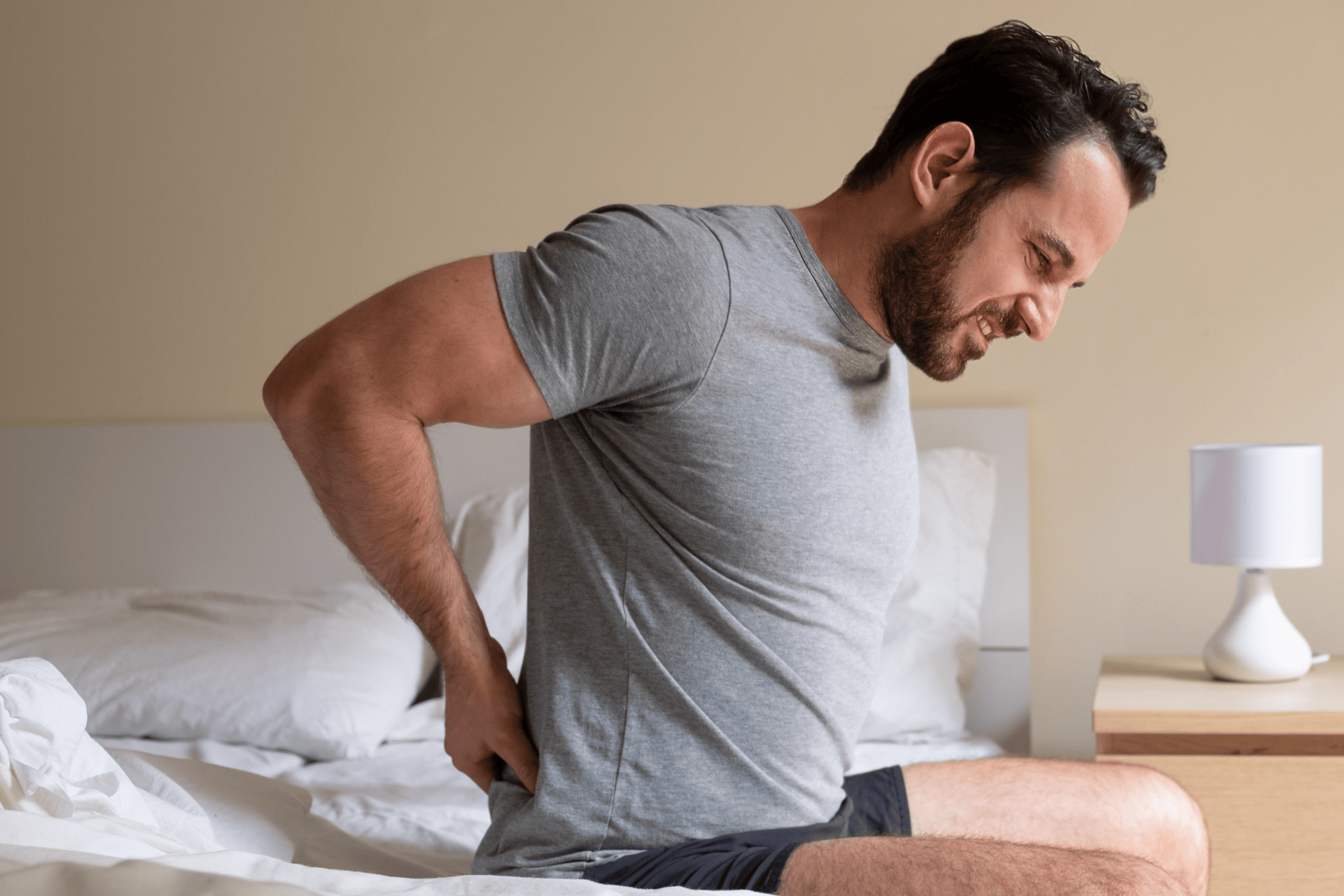 A Man sitting on a bed holding his lower back in pain