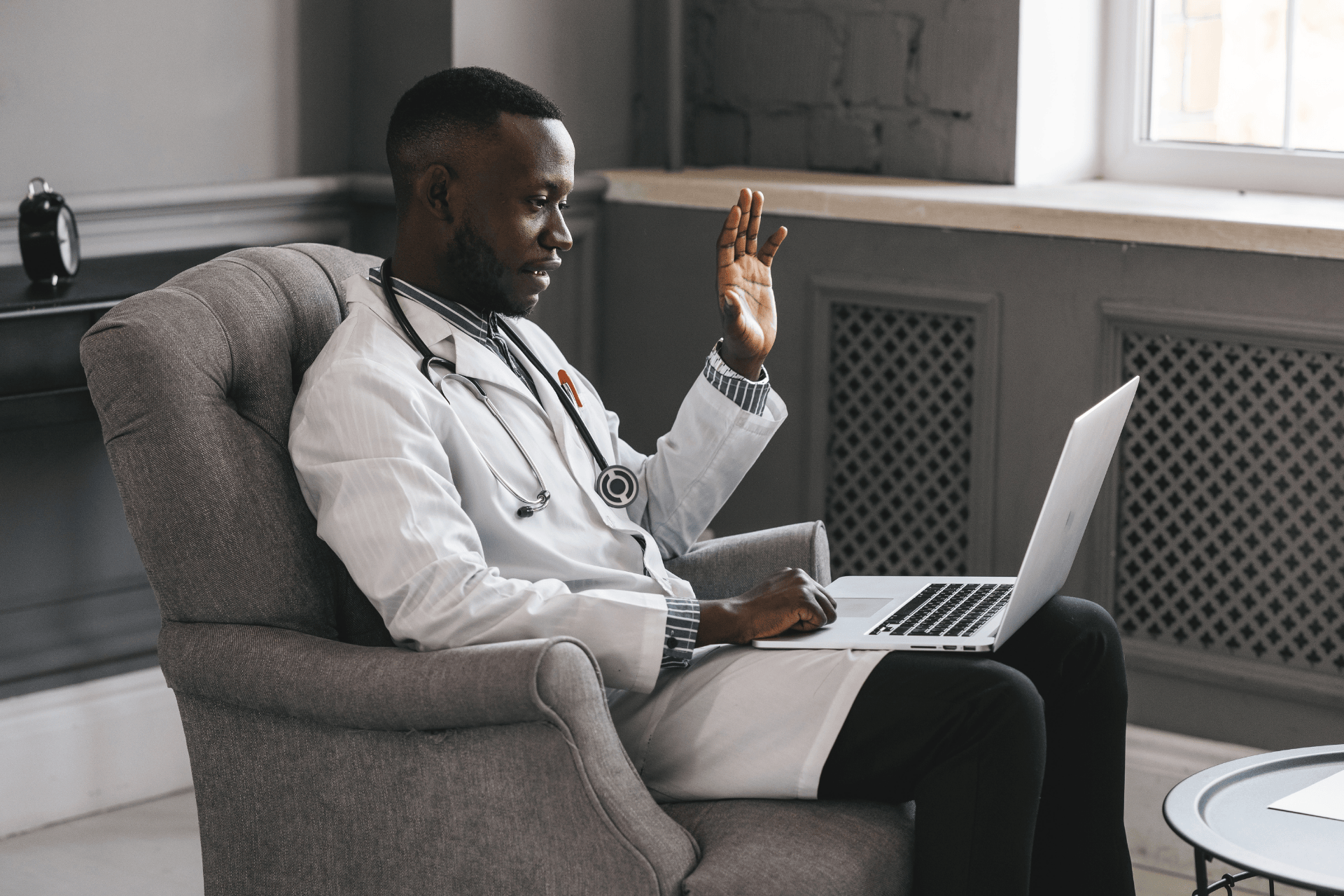 Doctor sitting in a chair waving during an online video call.