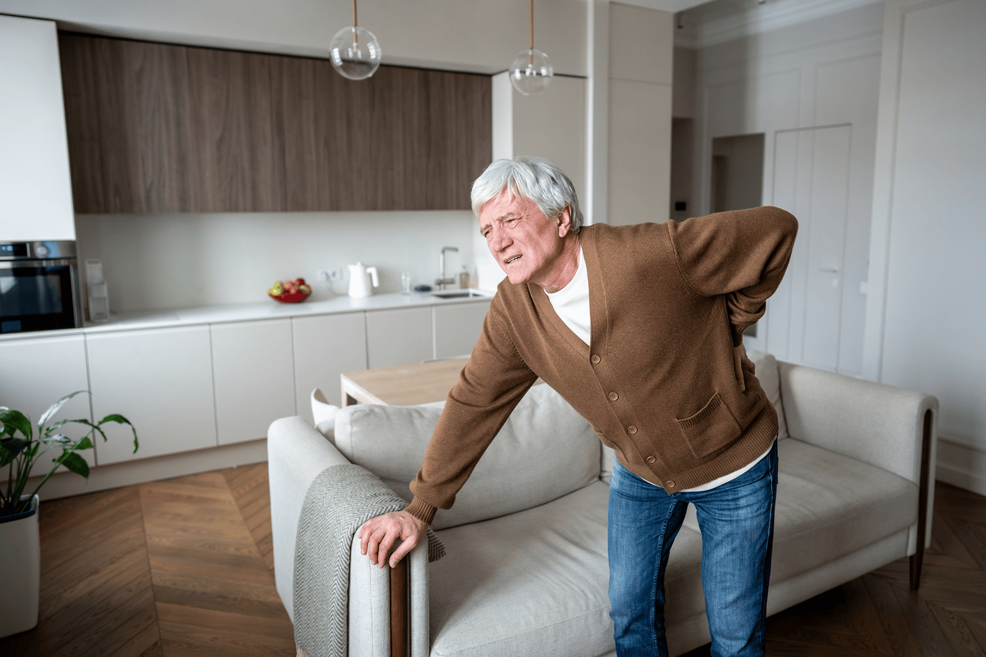 An Elderly man standing and holding his lower back in pain at home.