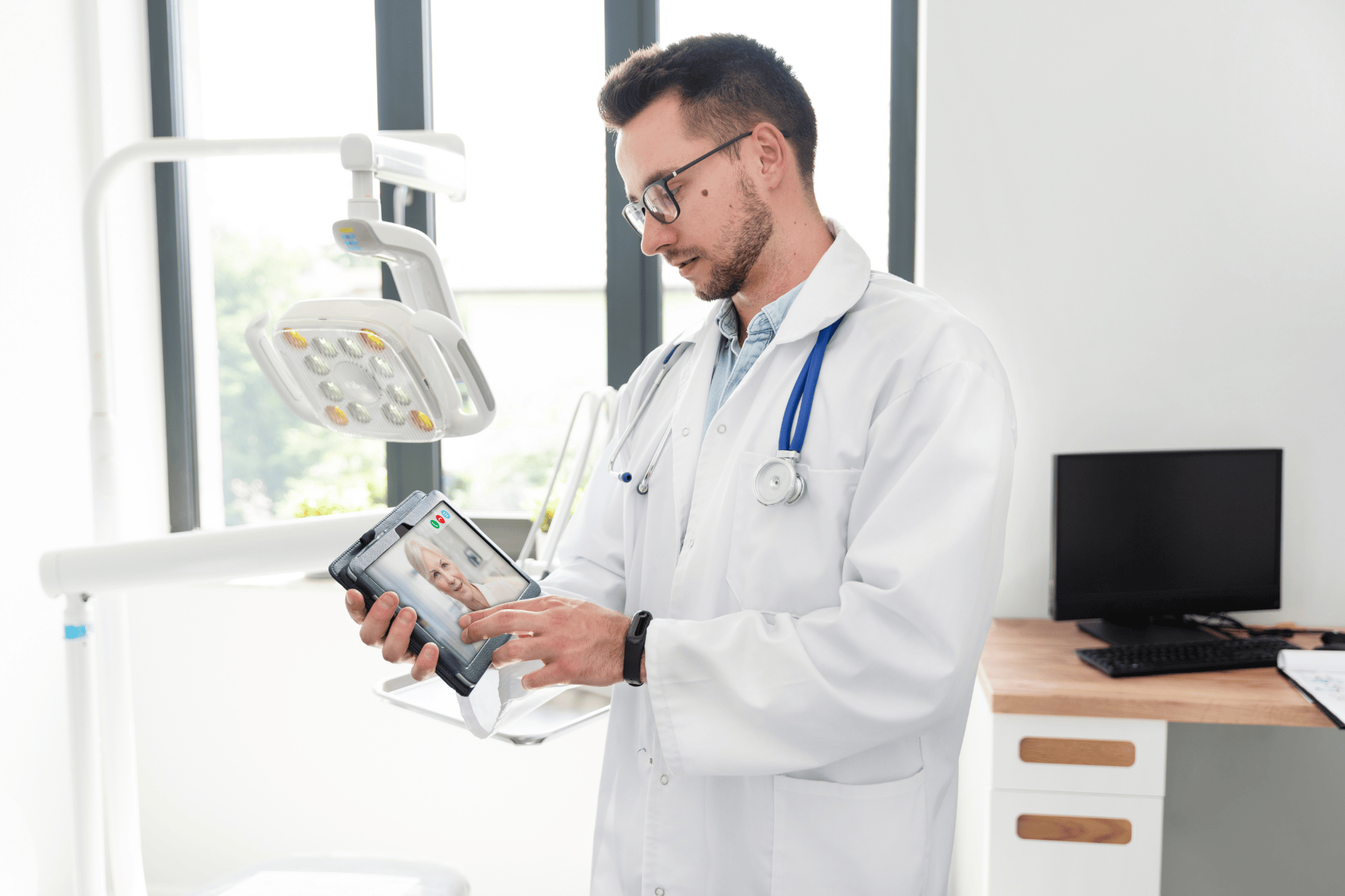 Doctor holding a tablet and talking to a patient on a video call in a clinic.