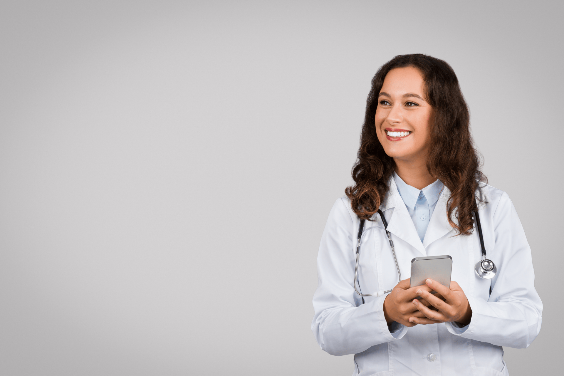 Smiling doctor holding a smartphone and looking to the side.