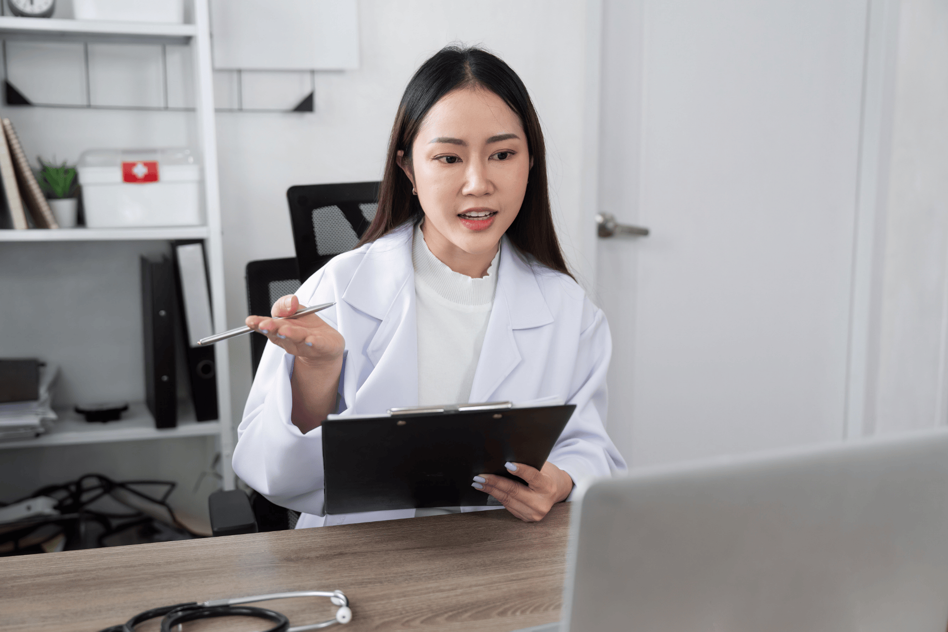 Female doctor holding a clipboard and talking during an online consultation.
