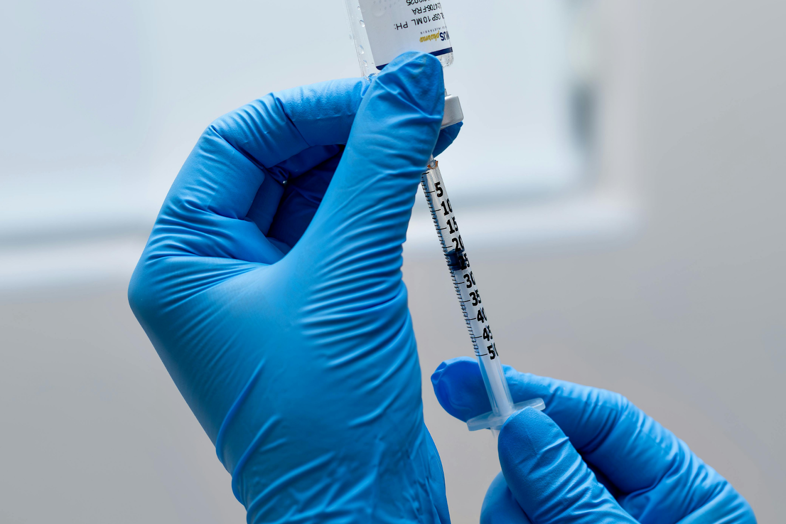 Gloved hands drawing liquid medication into a syringe from a vial.