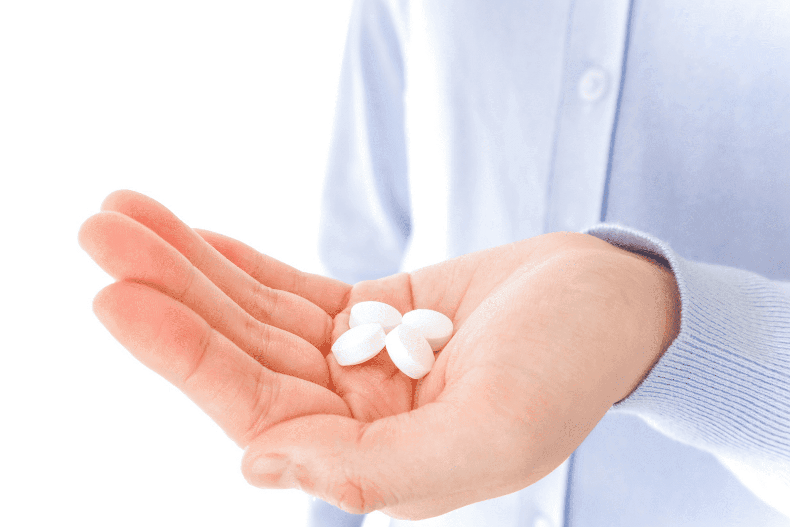 Hand holding several white tablets against a light background.