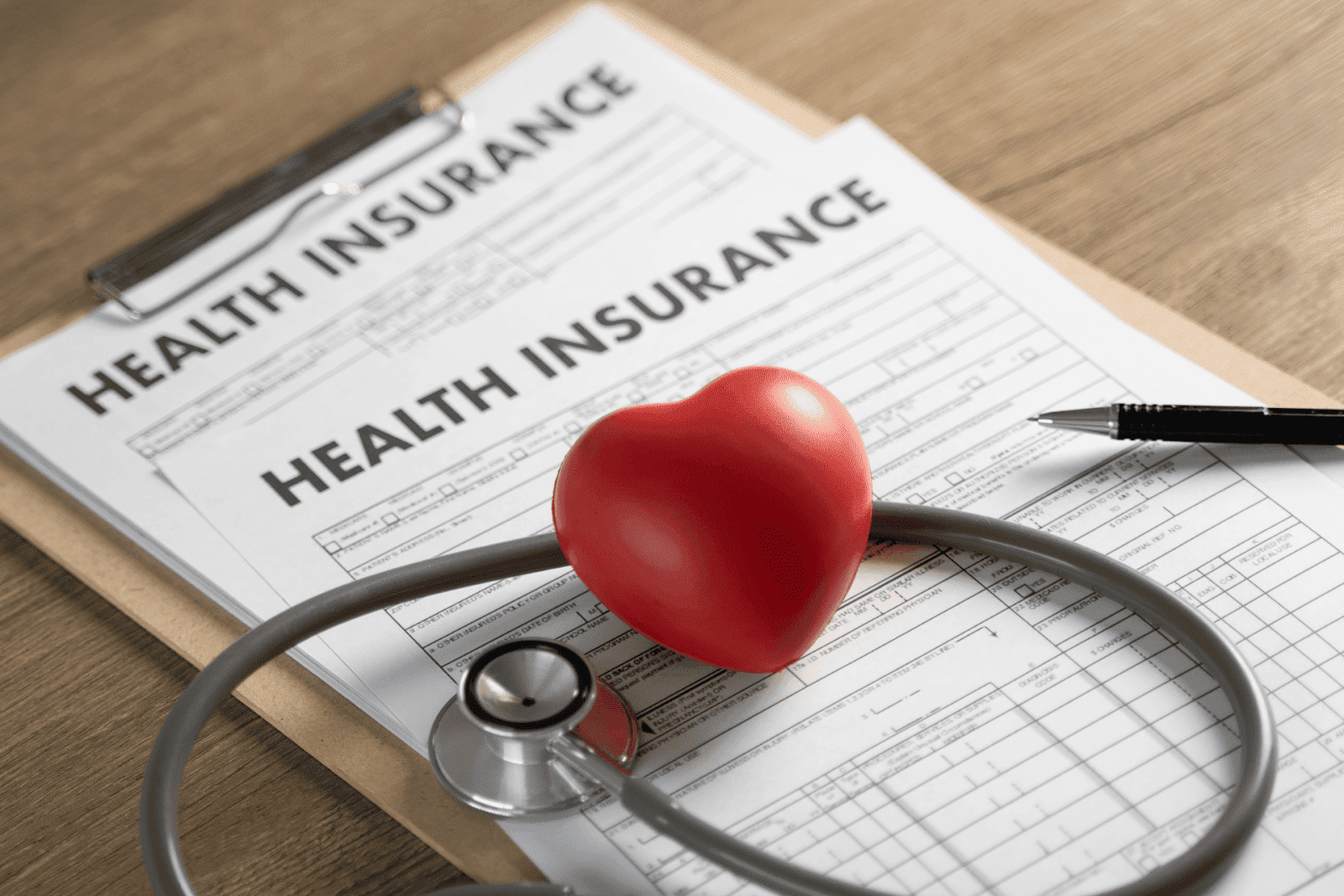 Health insurance paperwork on a clipboard with a stethoscope and red heart model on top