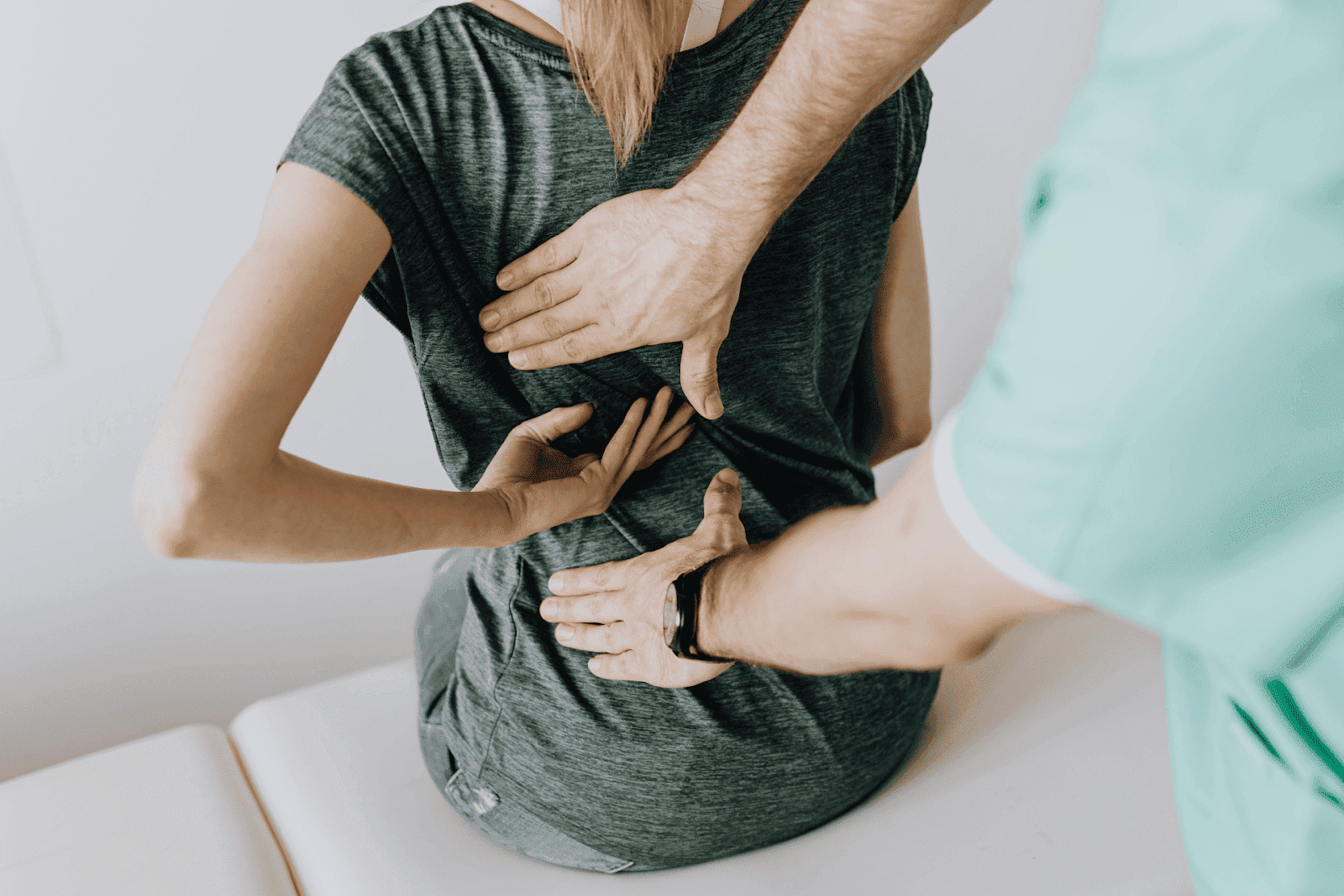 Healthcare professional examining a woman's back while she indicates areas of pain with her hands.