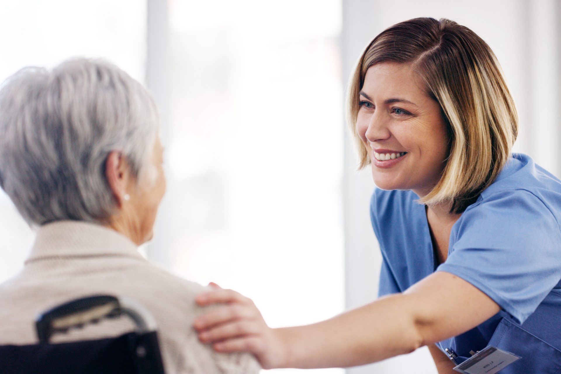 Healthcare worker smiling as they reassure an elderly patient seated in a wheelchair