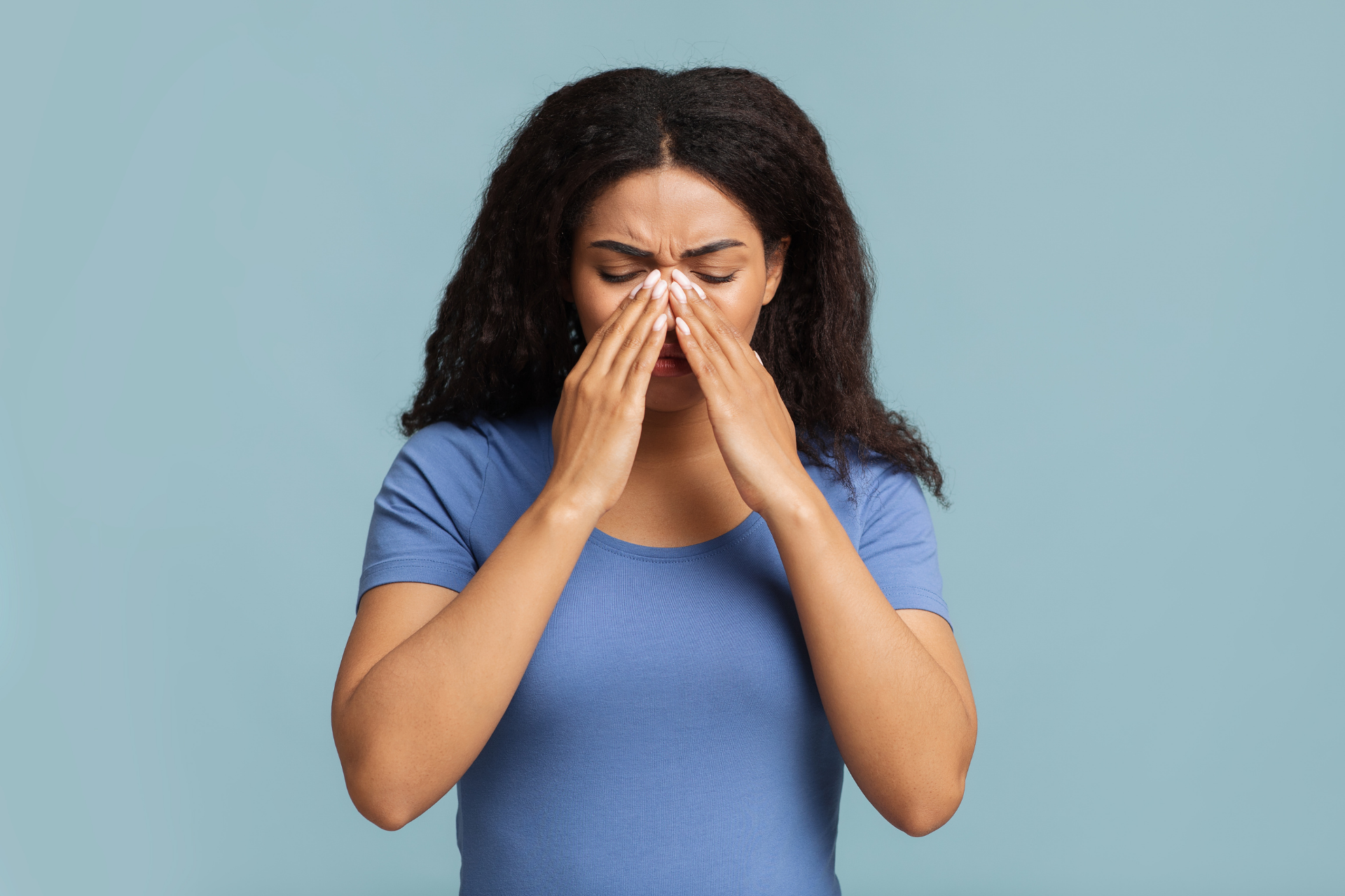 A woman pressing her nose and closing her eyes, appearing to have sinus pressure or nasal congestion