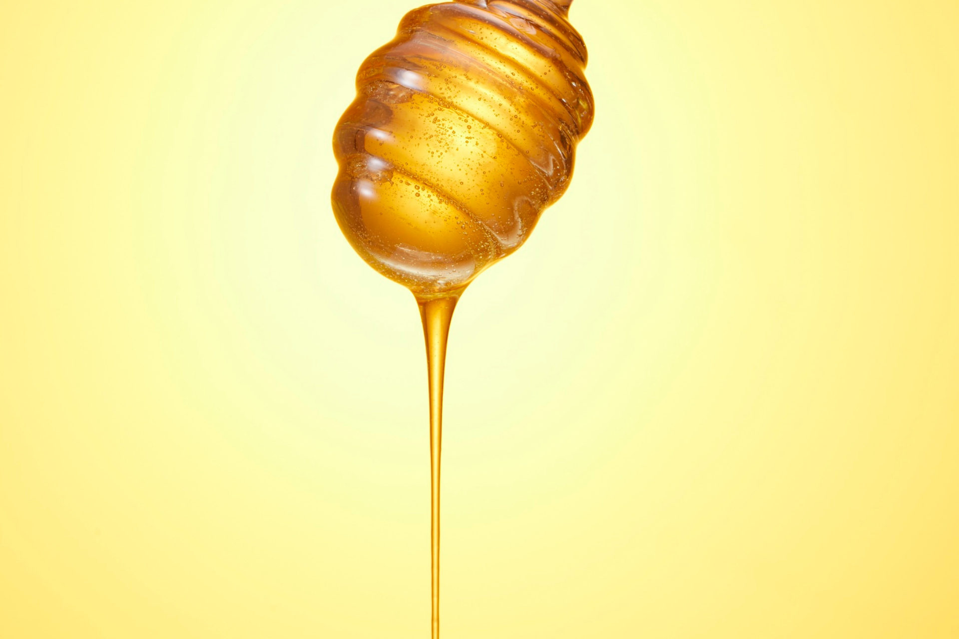 Honey dripping slowly from a honey dipper against a yellow background