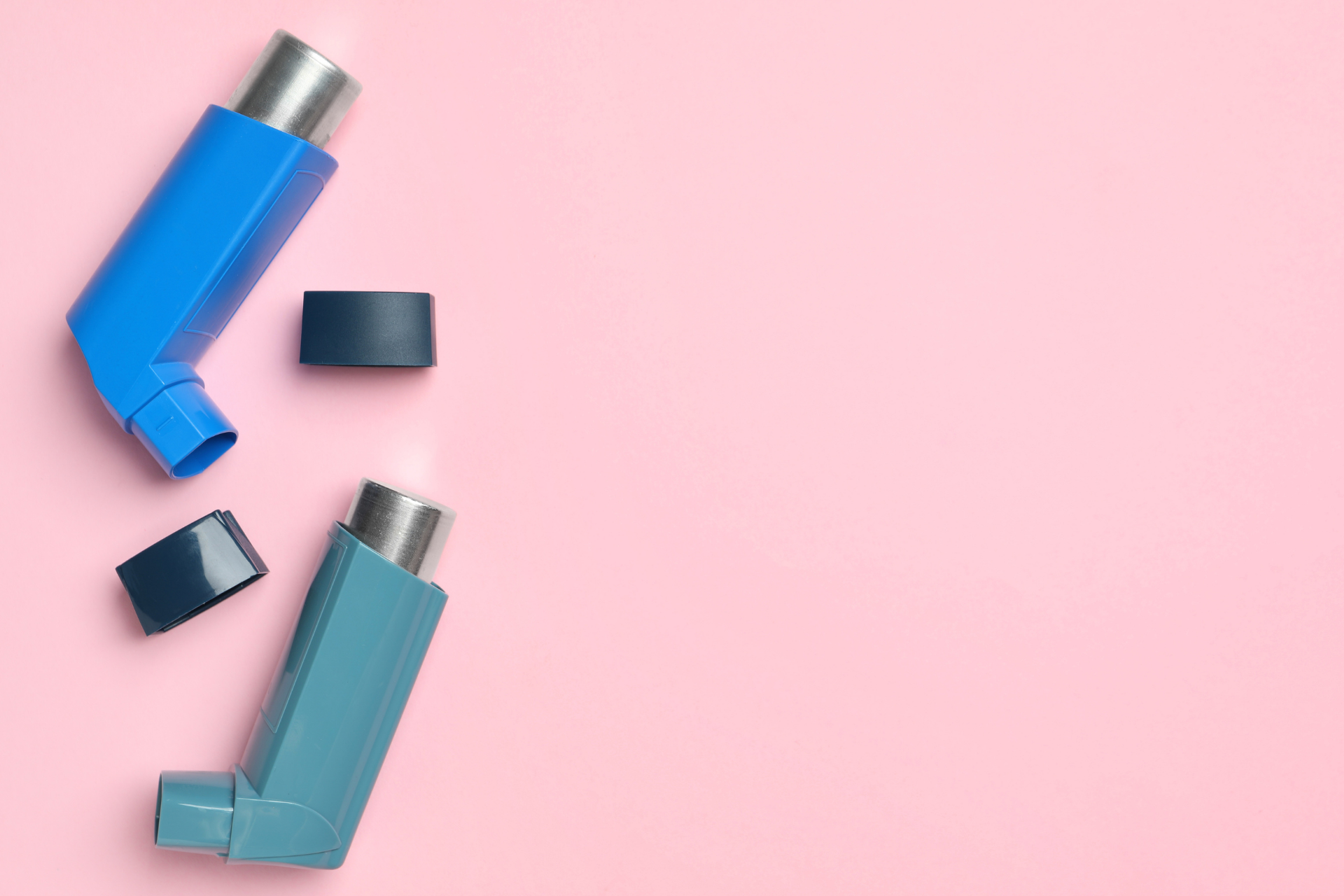 Two asthma inhalers with their caps off on a pink background
