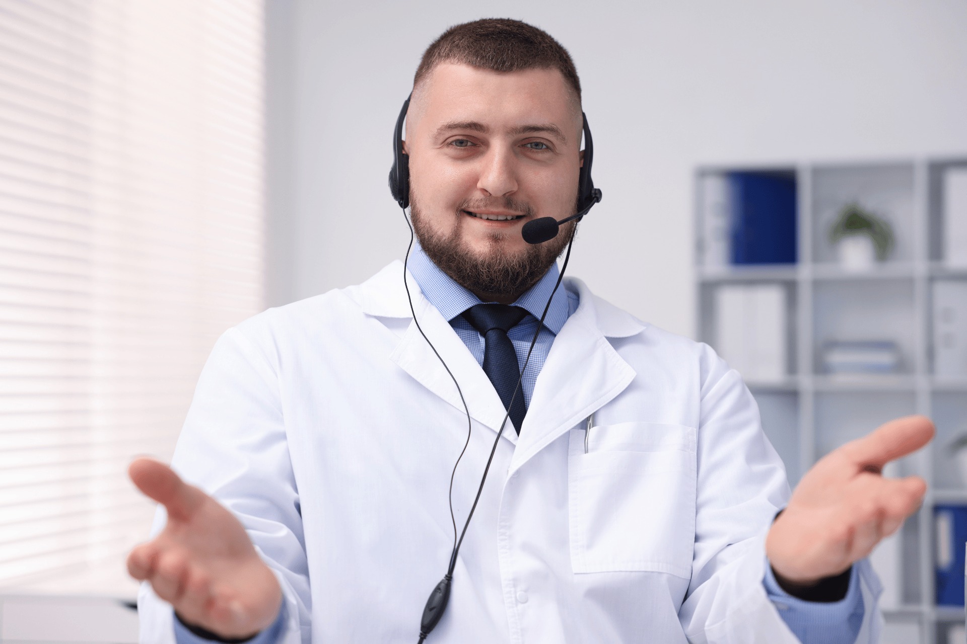 Male doctor wearing a headset, smiling with open hands.