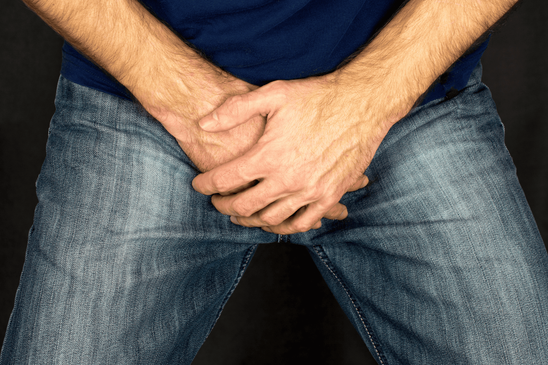 Man clutching his groin area in discomfort while wearing jeans.