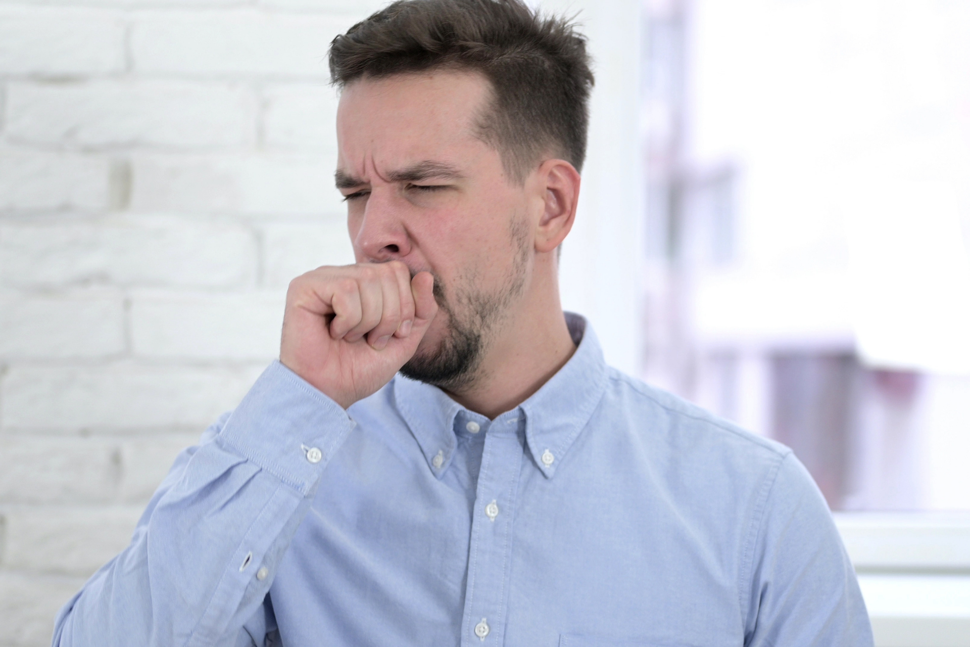 Man coughing into his hand, appearing unwell