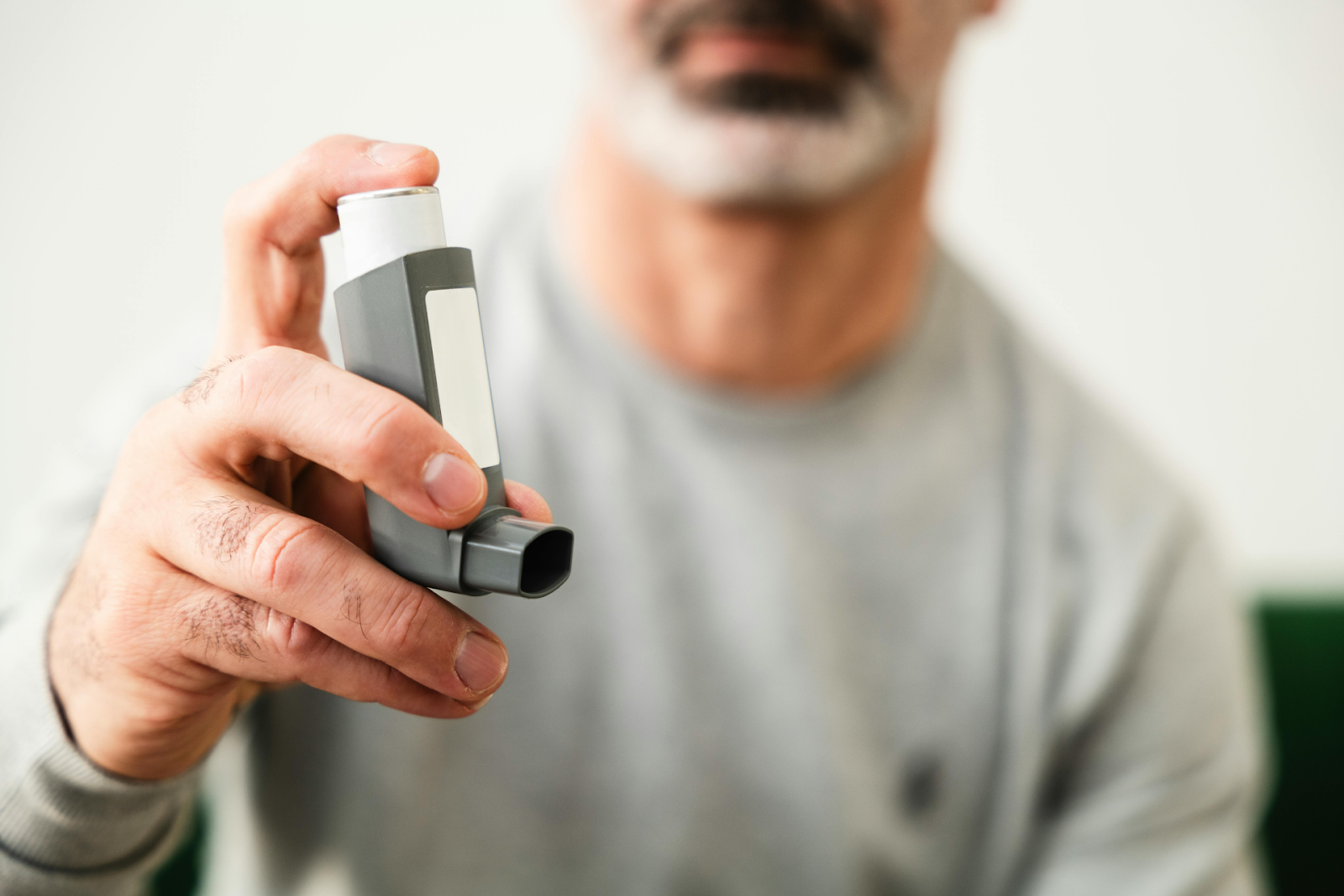 An adult man holding a gray asthma inhaler toward the camera