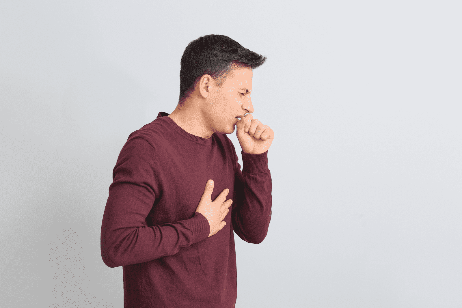 Man in a maroon sweater holding his chest and coughing.