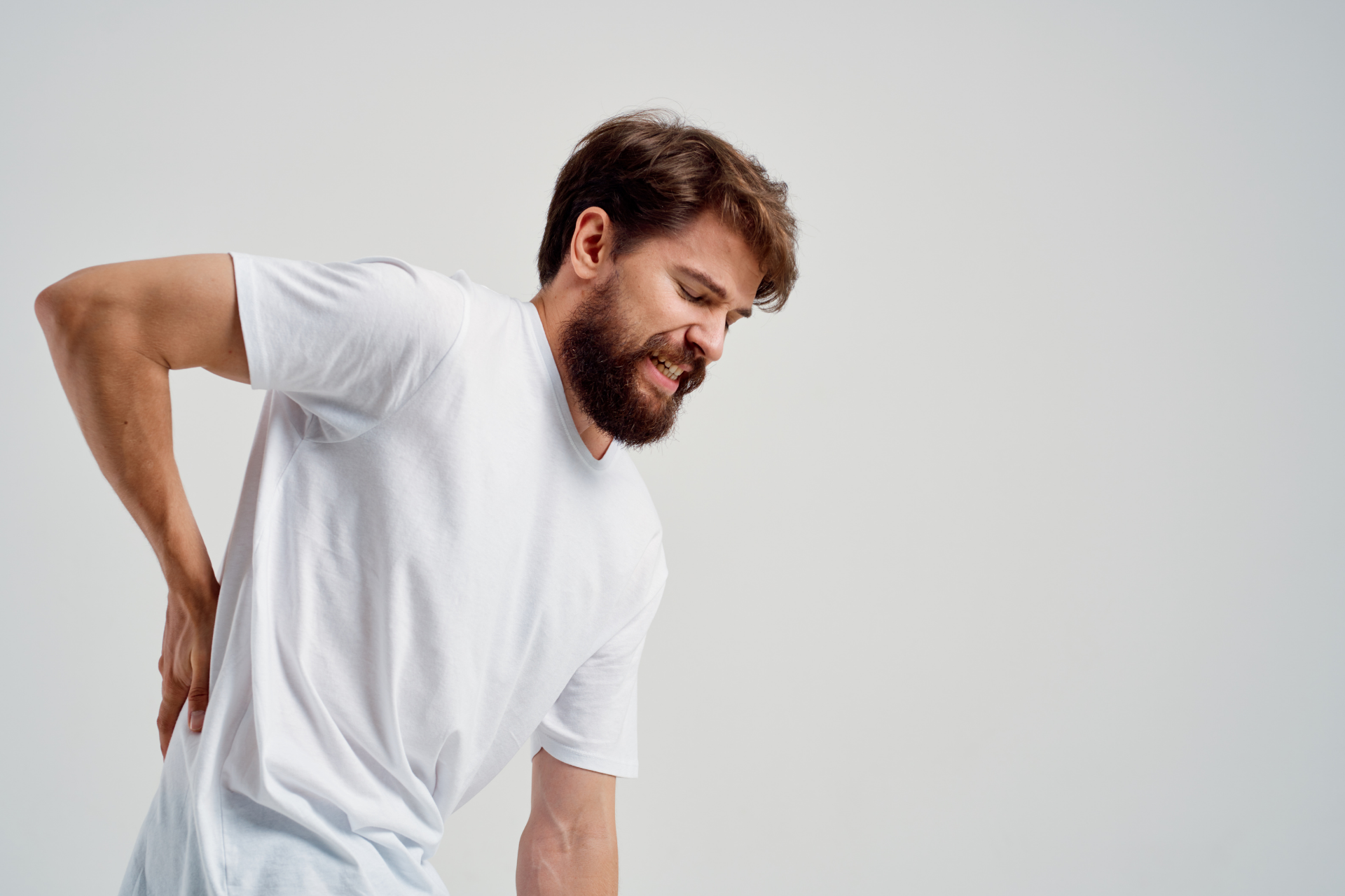 Man in a white shirt, grimacing and holding his lower back in pain