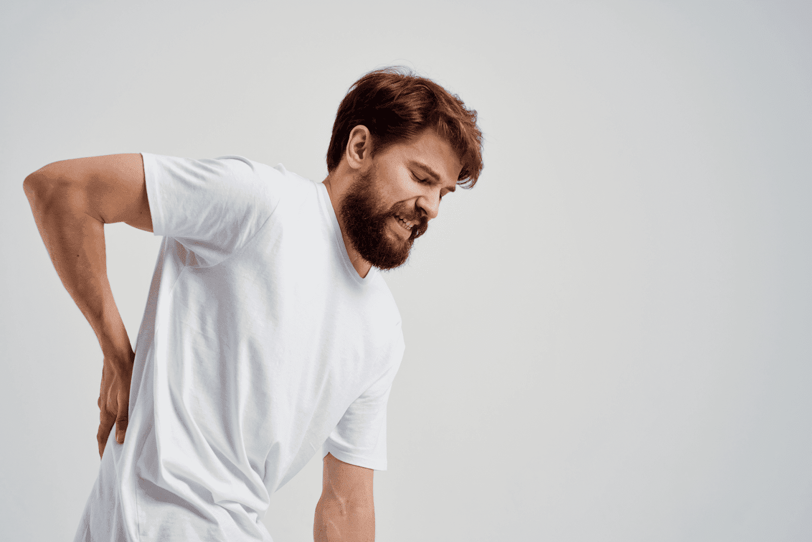 Man in a white shirt holding his lower back and wincing in pain.