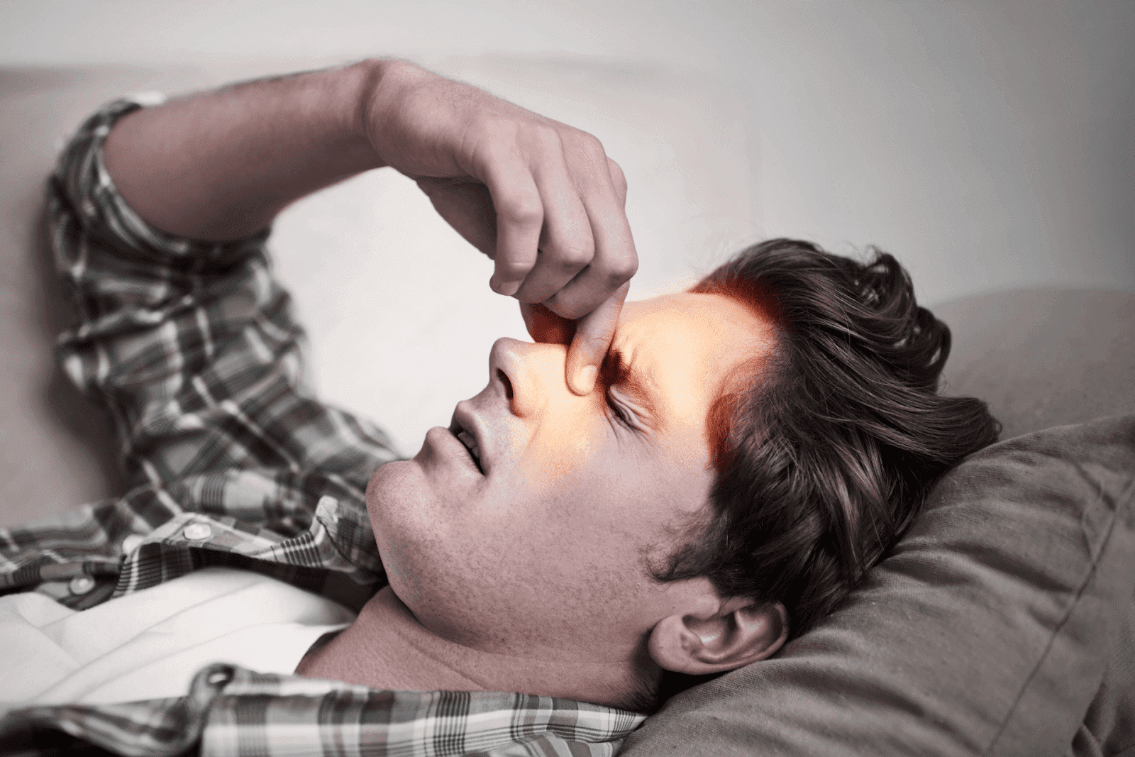 Man lying on couch pressing his nose and forehead, showing sinus pain