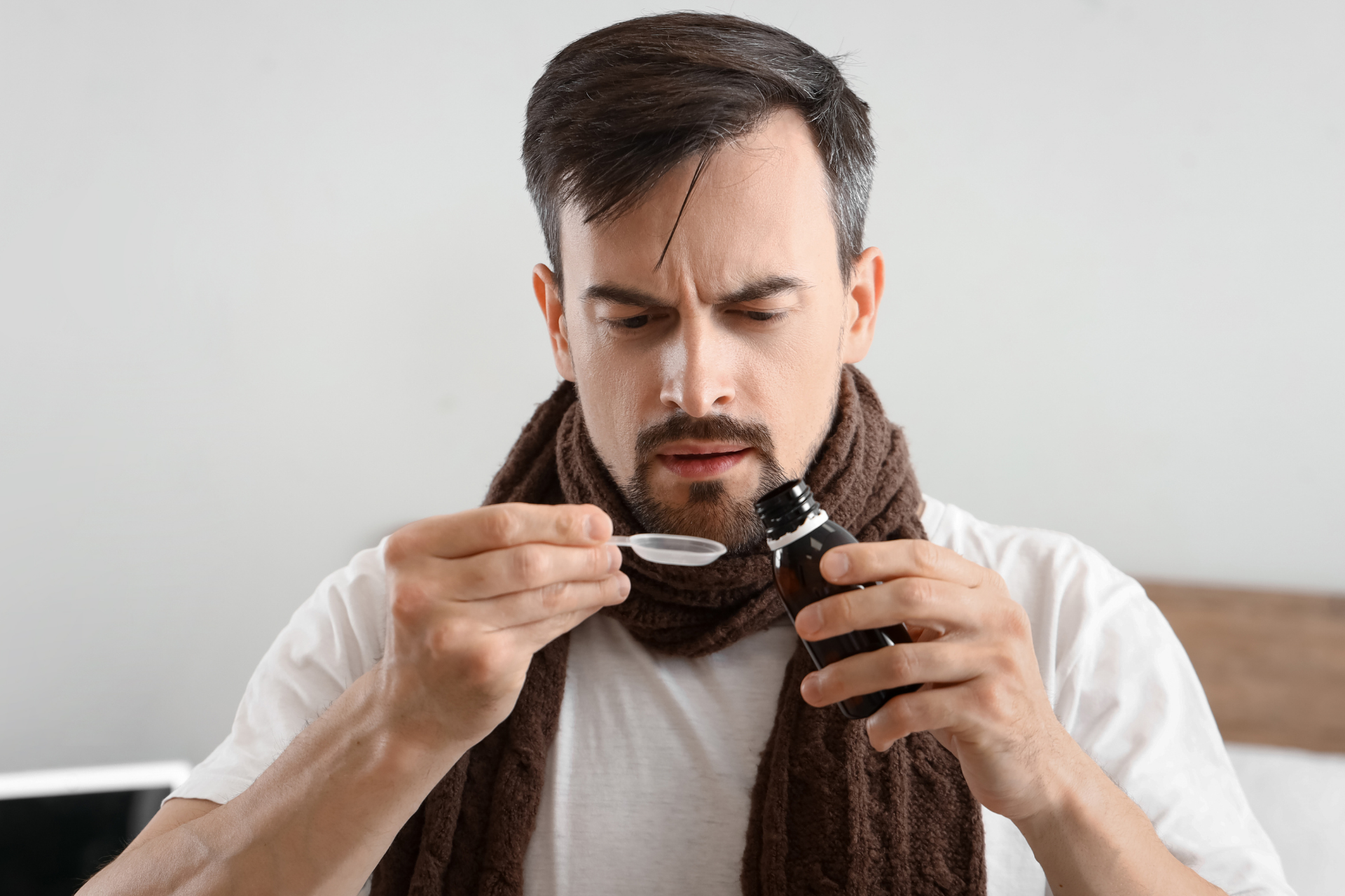 Man measuring cough syrup with a dosing spoon before taking medication