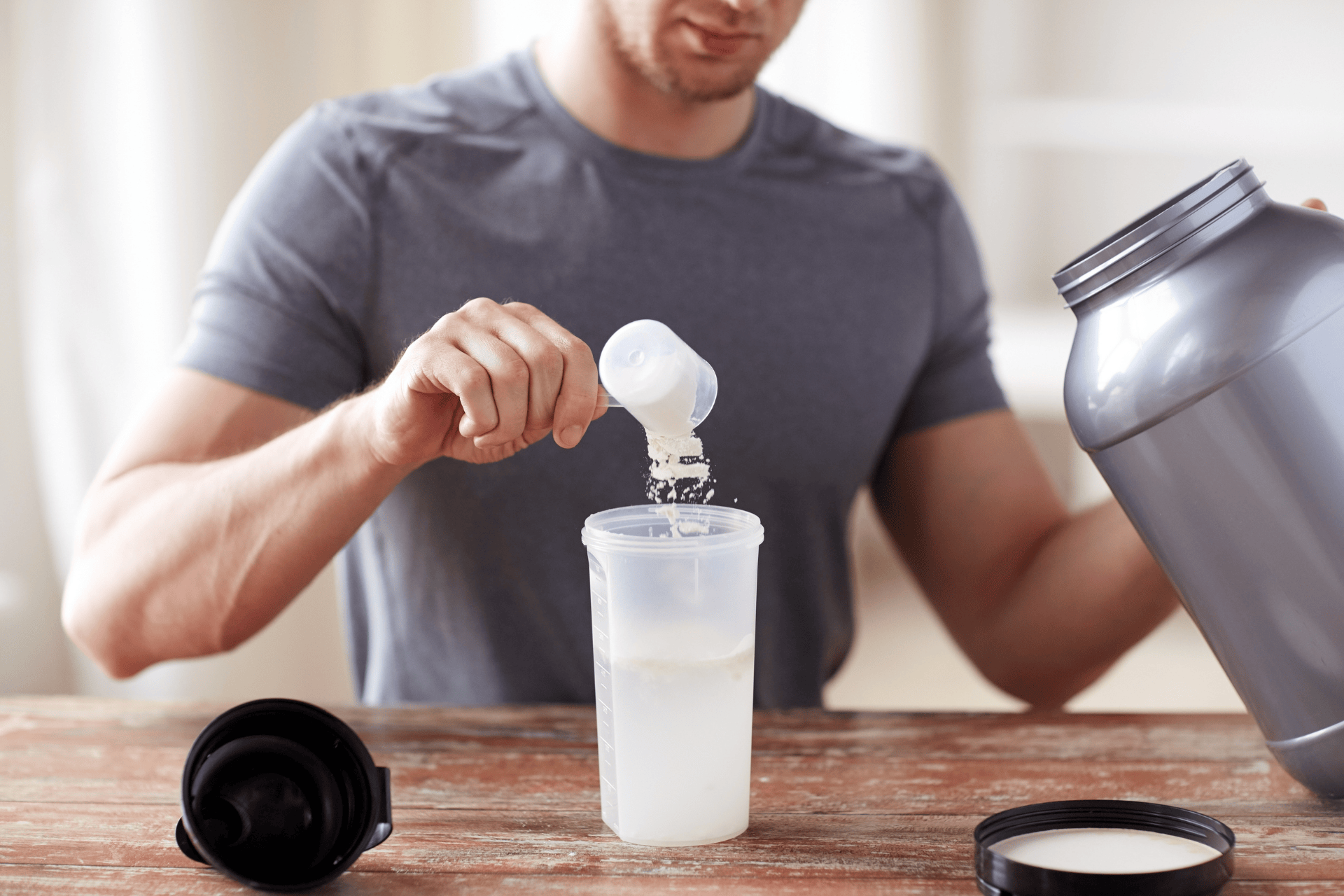 Man preparing a protein shake by adding powder to a shaker bottle.