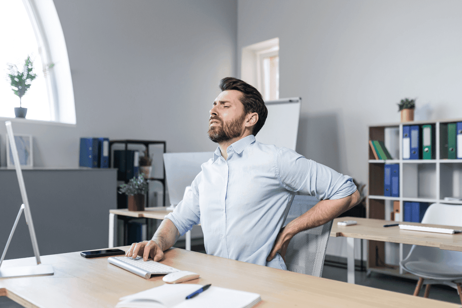Man sitting at a desk, holding his lower back in pain