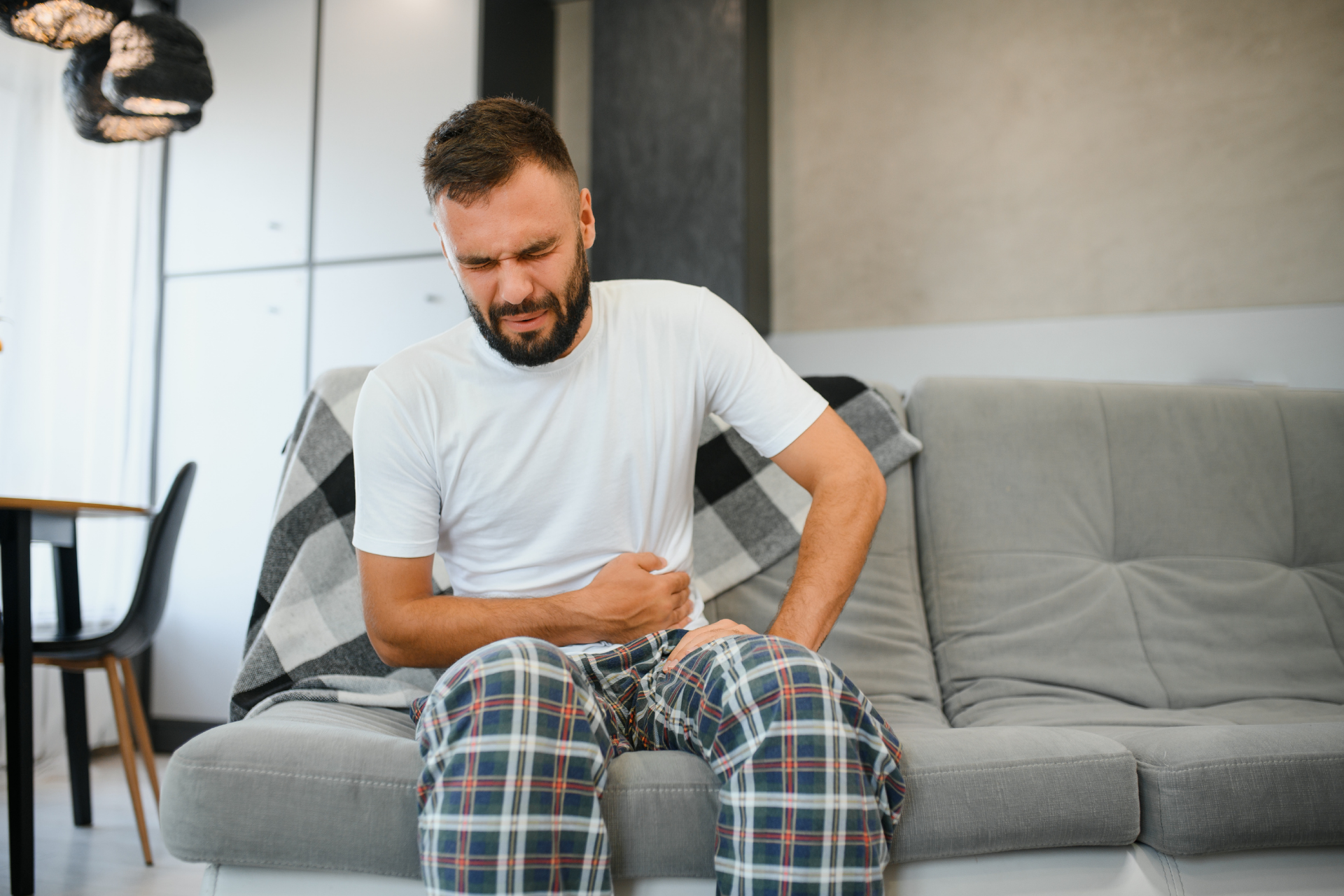 A man sitting on a couch holding his abdomen in pain