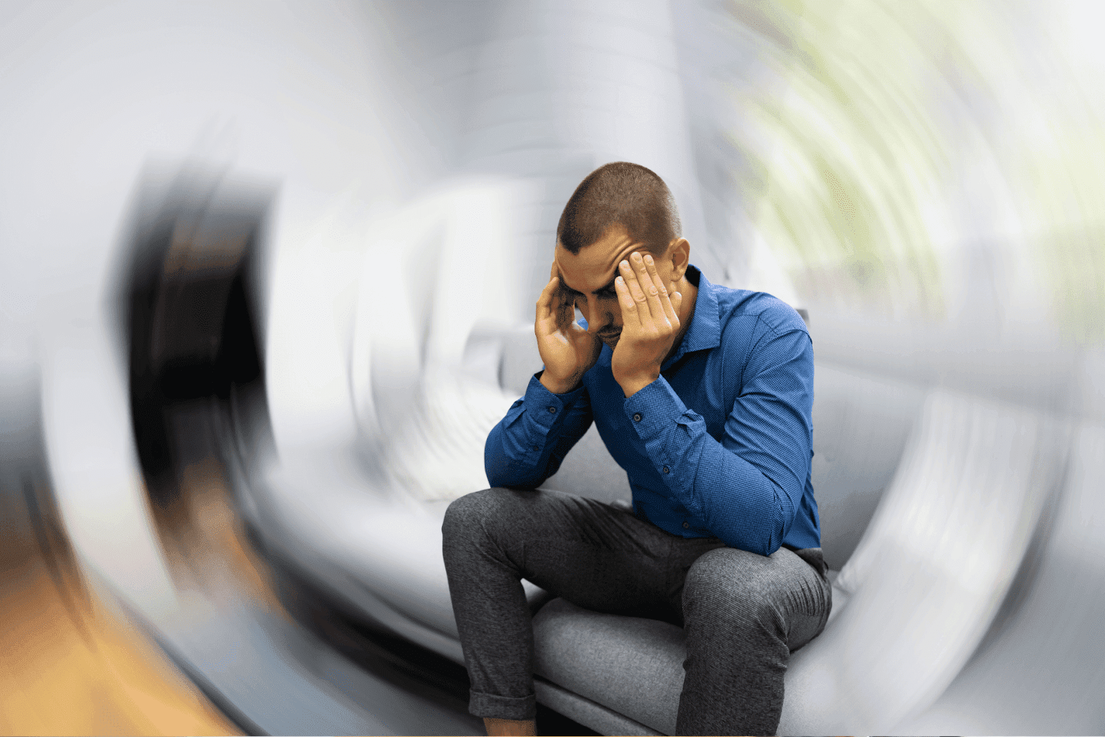 Man sitting with hands on head, experiencing dizziness with blurred background effect.